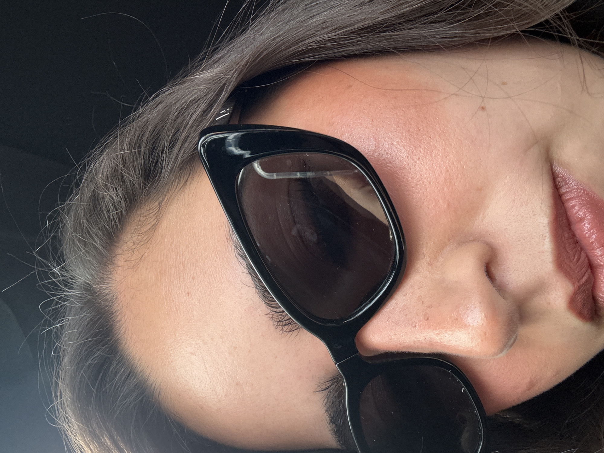 Close-up of a woman's face, featuring sunglasses. The woman has dark hair and fair skin. The sunglasses have a black frame and dark lenses. The background is blurry and dark. The location and context of the image (Heroica Puebla de Zaragoza, Mexico) are not discernible from the visual information provided.
