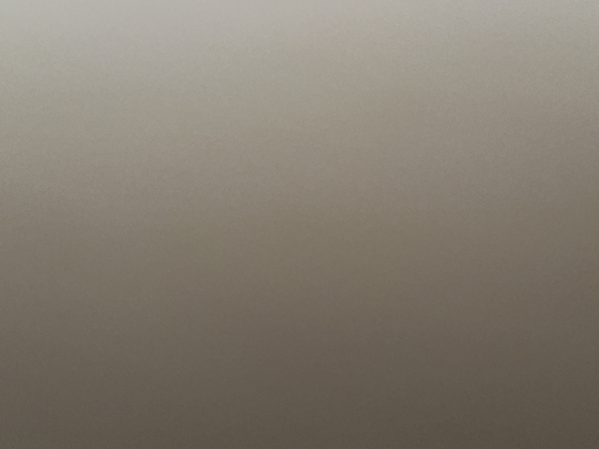 The image is a plain, neutral background, likely a wall or a large surface. There are no discernible objects, people, or actions depicted. The lighting appears to be uniform with a slight gradient towards the right side, suggesting ambient light from a window or artificial source. The color is a muted taupe or beige. There is no context provided to suggest a specific location in Belgrade, Serbia, or any other place.
