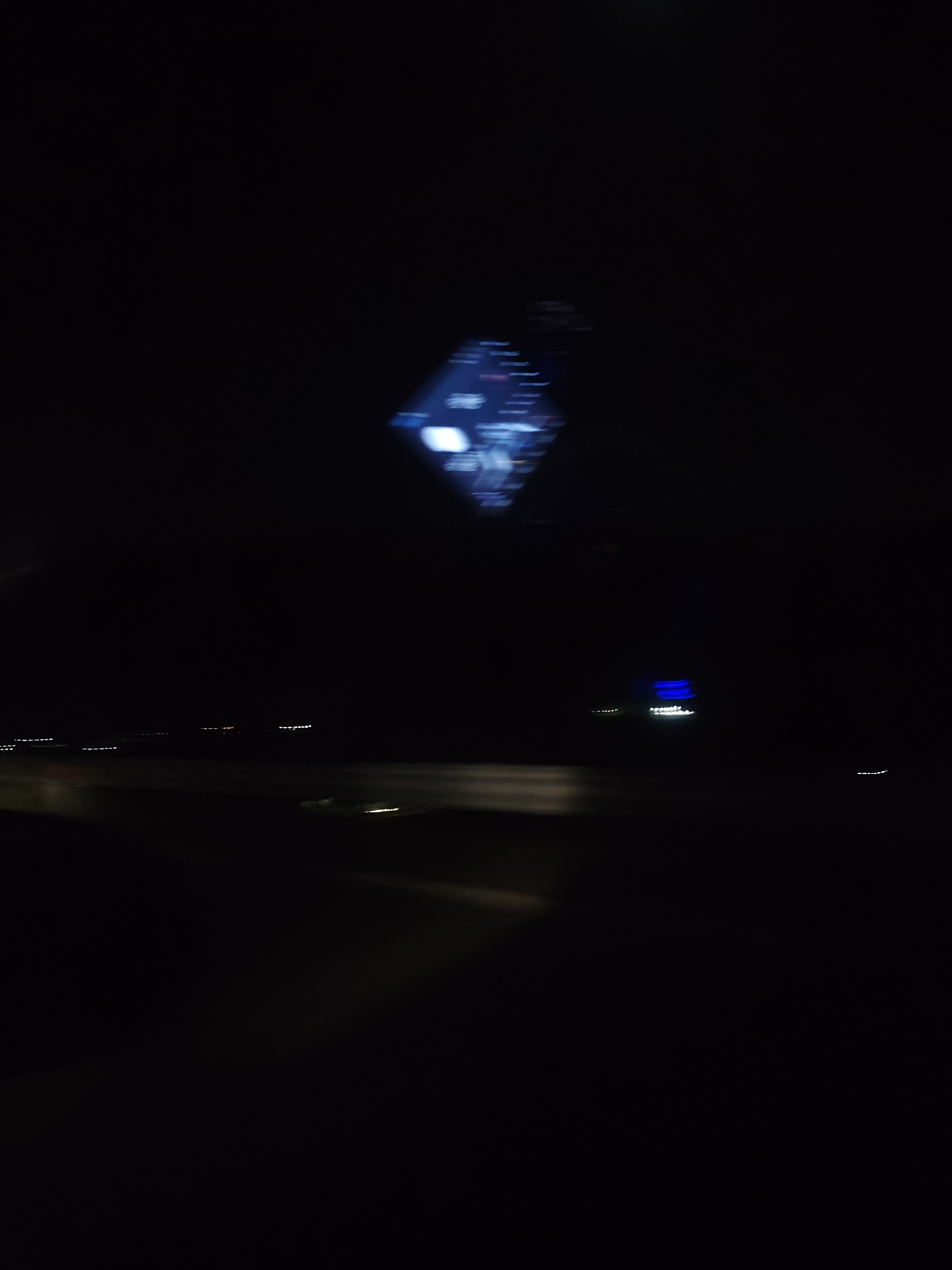 The image appears to be taken from inside a vehicle at night. The blurry lights of a car's dashboard are visible in the top center of the image. Outside, there's a blurry view of a road, along with the lights of other vehicles and buildings. It is not possible to ascertain the location in the city of Jeleznitsa, Bulgaria.
