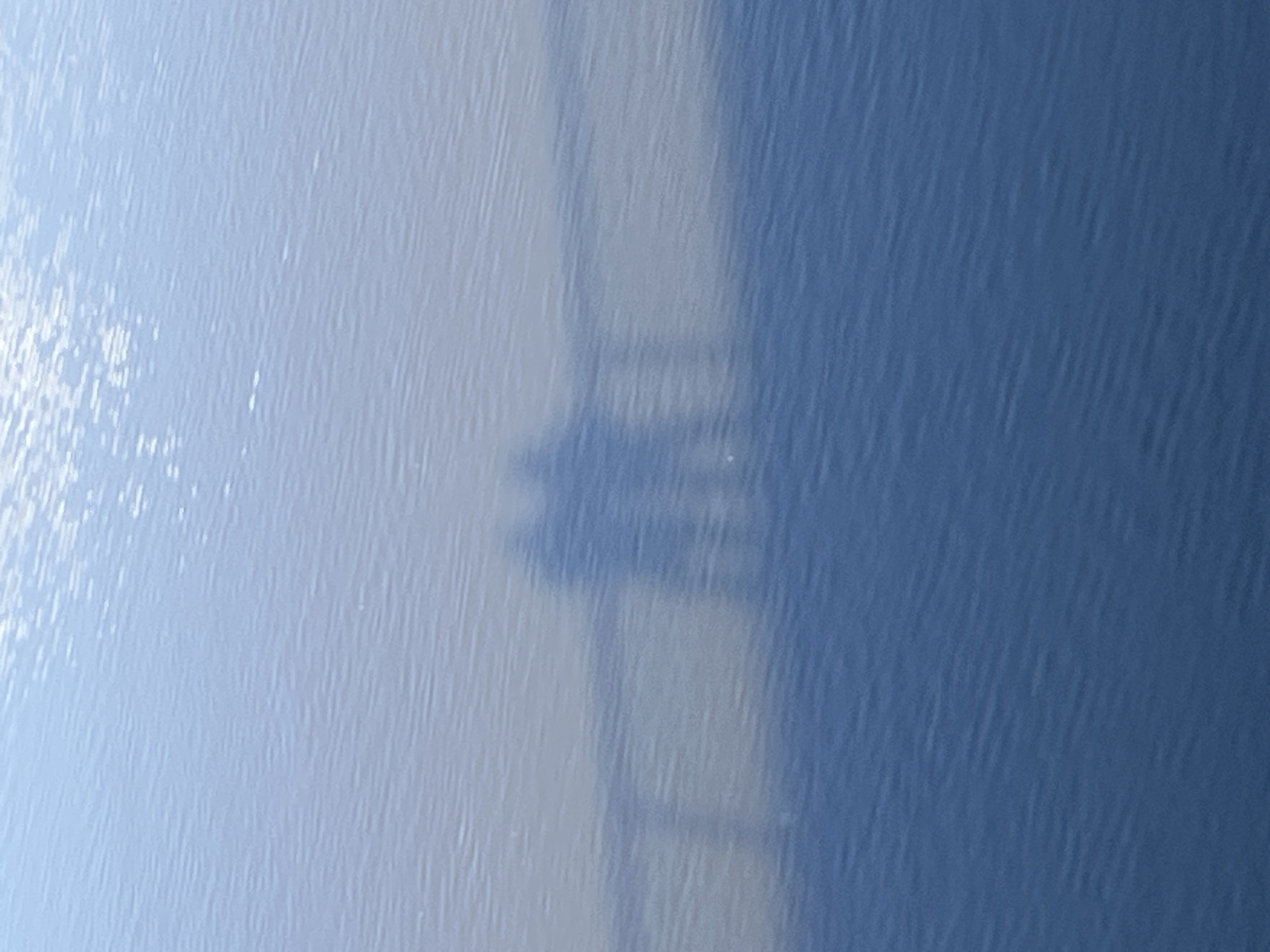 A shadow of a figure standing on a ladder or scaffolding is cast against a light blue and dark blue surface. The photograph was taken in Saarburg, Germany.