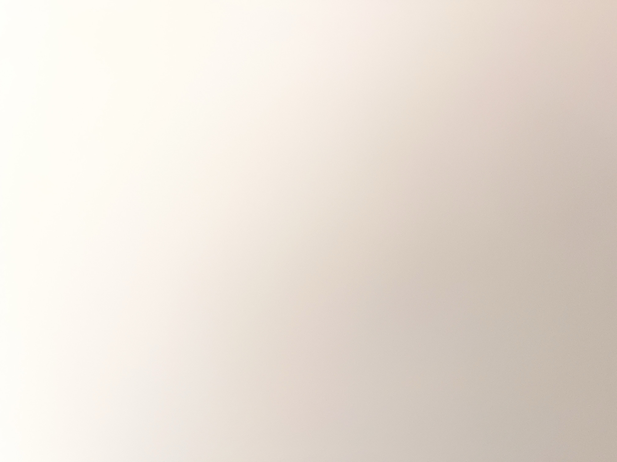 The image is an abstract, textured background. It appears to be a smooth surface with subtle variations in color and lighting, creating a gradient from a very light, almost white hue at the top to a slightly darker, beige or light brown tone at the bottom. The texture suggests a fine grain or a slight dappling, visible upon close inspection, possibly from the material of the surface or the lighting conditions. There are no discernible objects, people, or environmental features that would indicate a specific location within a city.