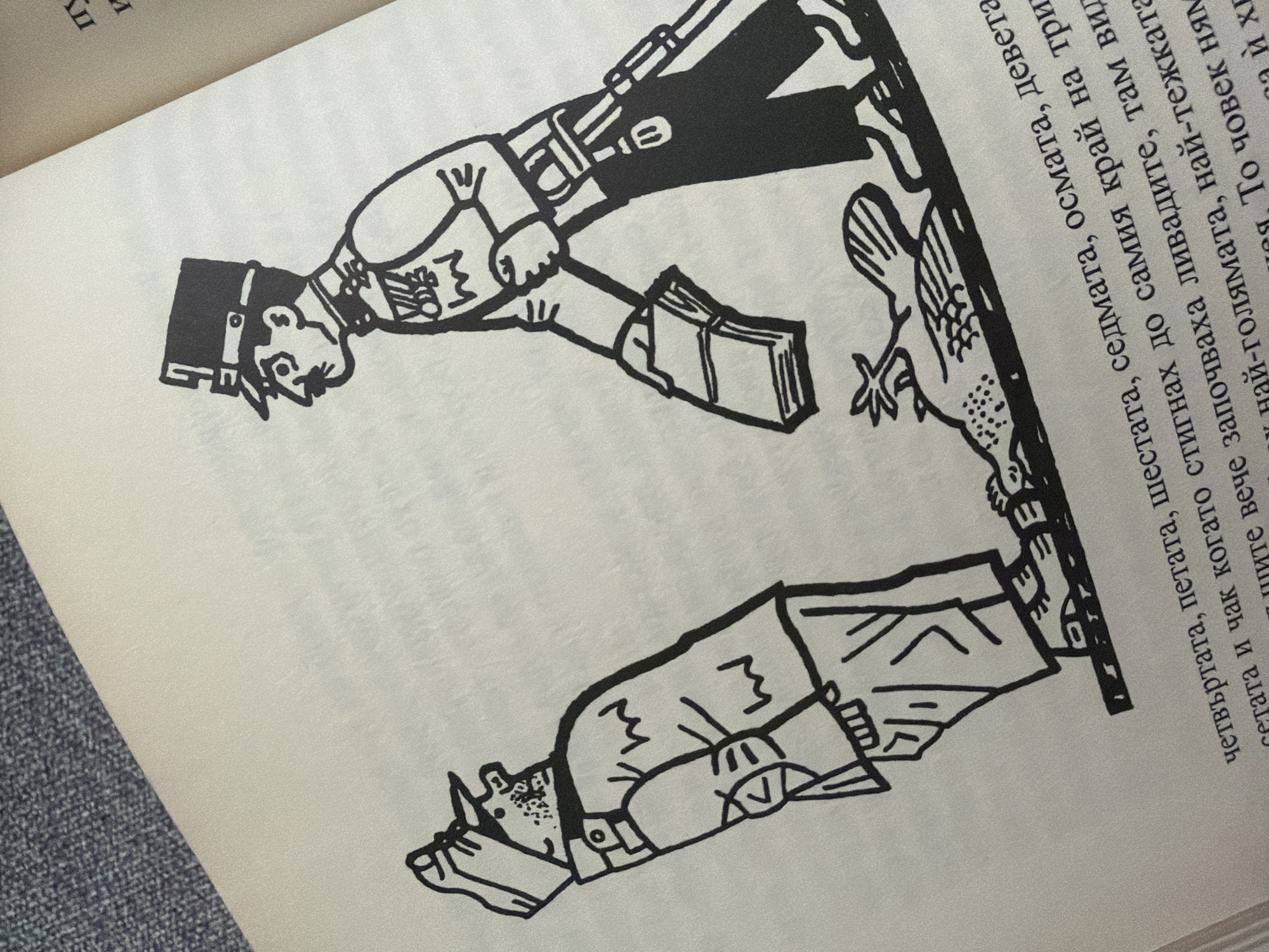 The image is a black and white ink drawing on a page of a book. The drawing depicts two men in military uniforms and a fallen bird on the ground. The man on the right is taller and appears to be in a position of authority, wearing a hat with a plume, a decorated jacket, and dark pants. He is holding a stack of papers or books in his left hand and has a sword or bayonet attached to his belt. The man on the left is shorter, also in a military uniform, and is looking upwards and to his right. He is wearing a cap and his posture suggests deference or surprise. A bird, depicted with its wings spread, lies on its side on the ground between the two figures, with some scattered debris around it. The bottom of the image contains text in a foreign language, likely Bulgarian, which is partially obscured by the drawing. The background is plain, indicating the drawing is the primary focus. There is no visual information within the image that provides any indication of the city of Pazardzhik, Bulgaria.