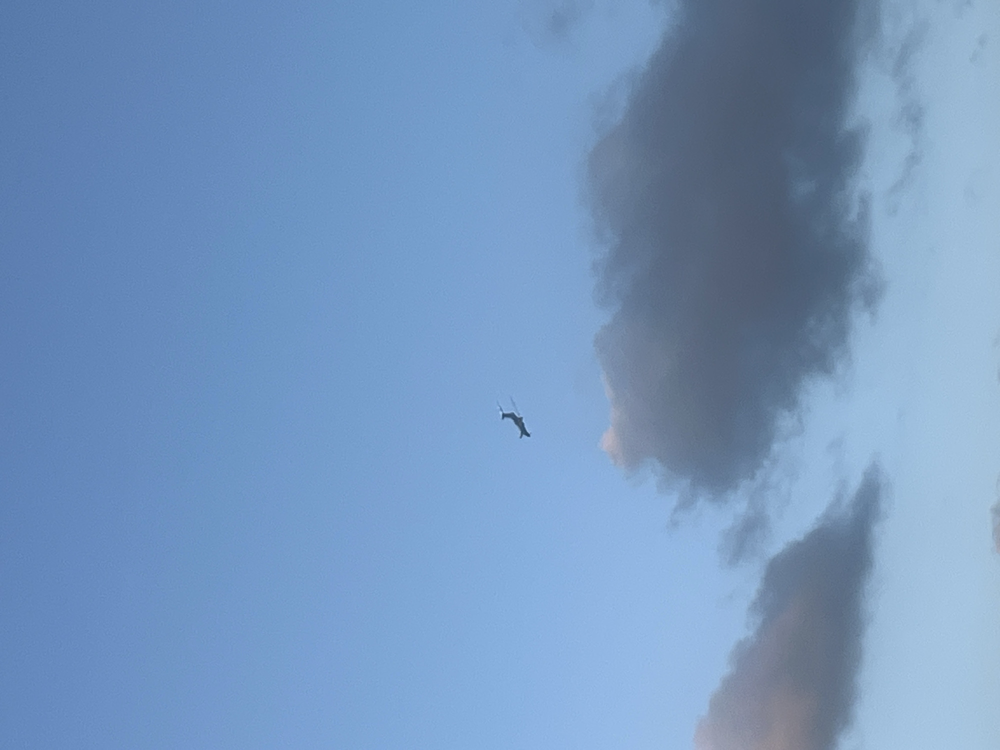 The image shows a clear blue sky with a few clouds, and a small airplane in flight. The airplane is silhouetted against the sky, and its wings and tail are visible. The clouds are dark and puffy, and they are located in the lower part of the image. The image was taken in Jacksonville, United States of America.