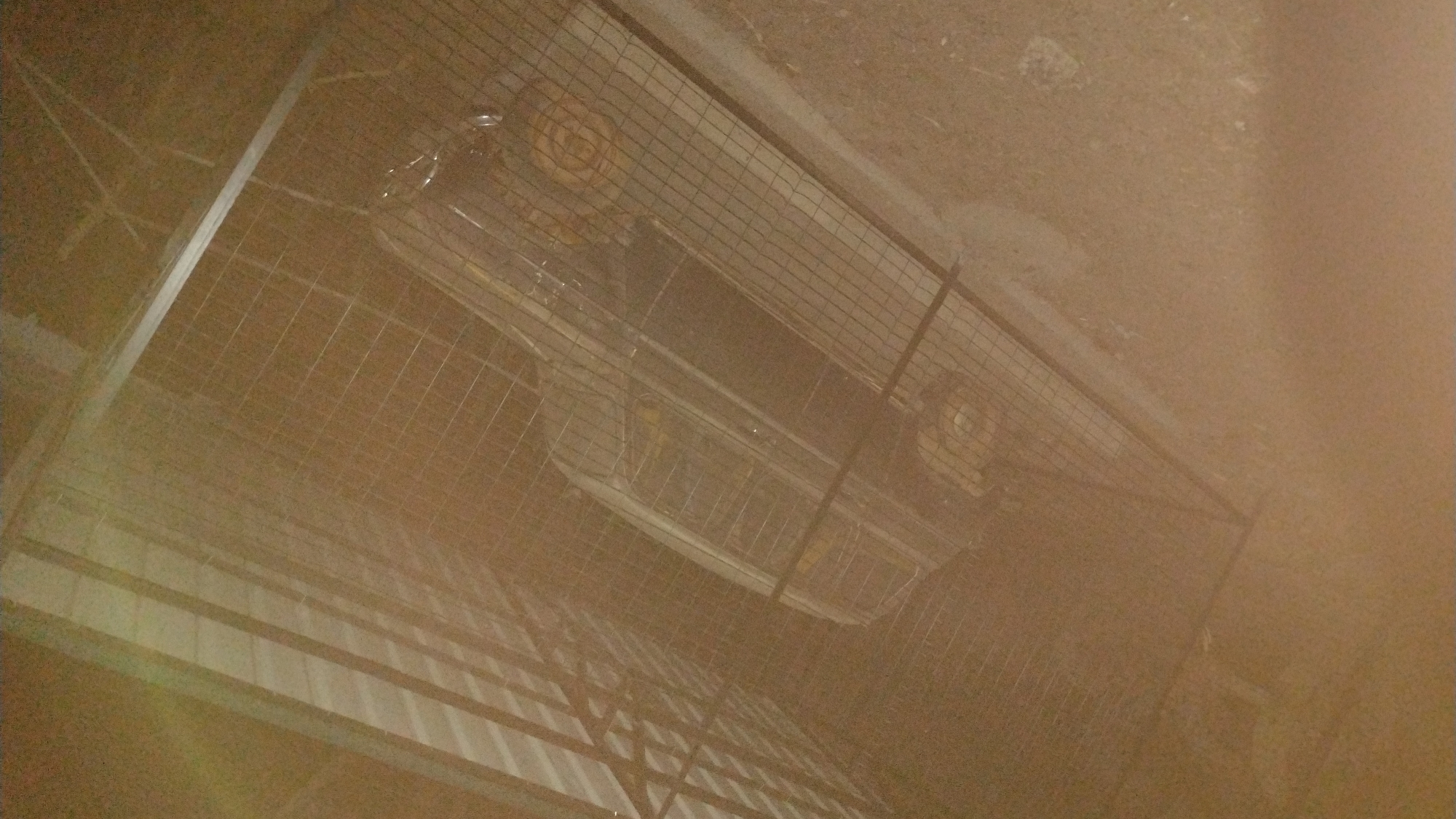A metal cage is situated outdoors on a dirt and concrete surface. Inside the cage, a portable heater is visible. The scene appears to be dusk or nighttime, indicated by low lighting and shadows. Details about the location in Jos, Nigeria, and the presence of people, actions, or interactions are not discernible from the provided image.