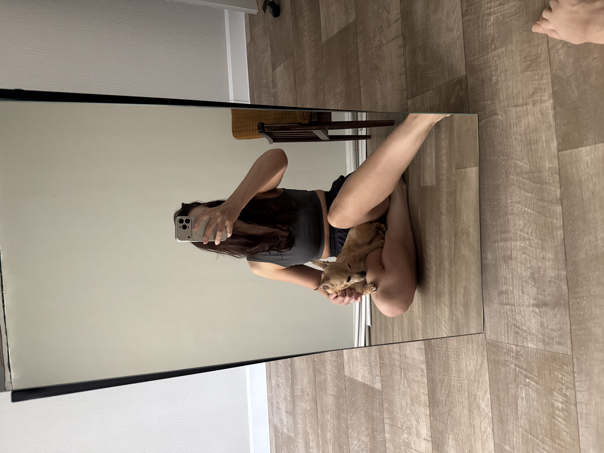 A mirror reflects a woman holding a dog while taking a selfie. The environment appears to be an indoor space with wood-look flooring. The location in Chaikovsky, Russia, is unknown.