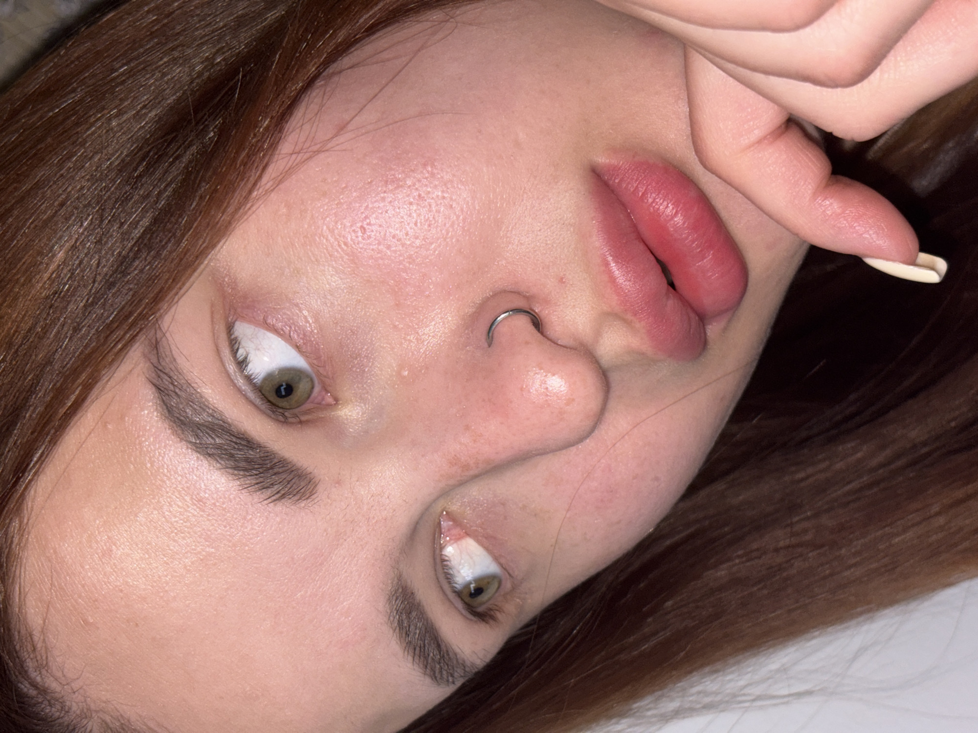 Close-up of a woman's face rotated at an angle. She has light skin, brown hair, and green eyes. A silver ring is visible in her left nostril. Her right hand is near her lips.
Port-Katon, Russia is not discernible in the image.
