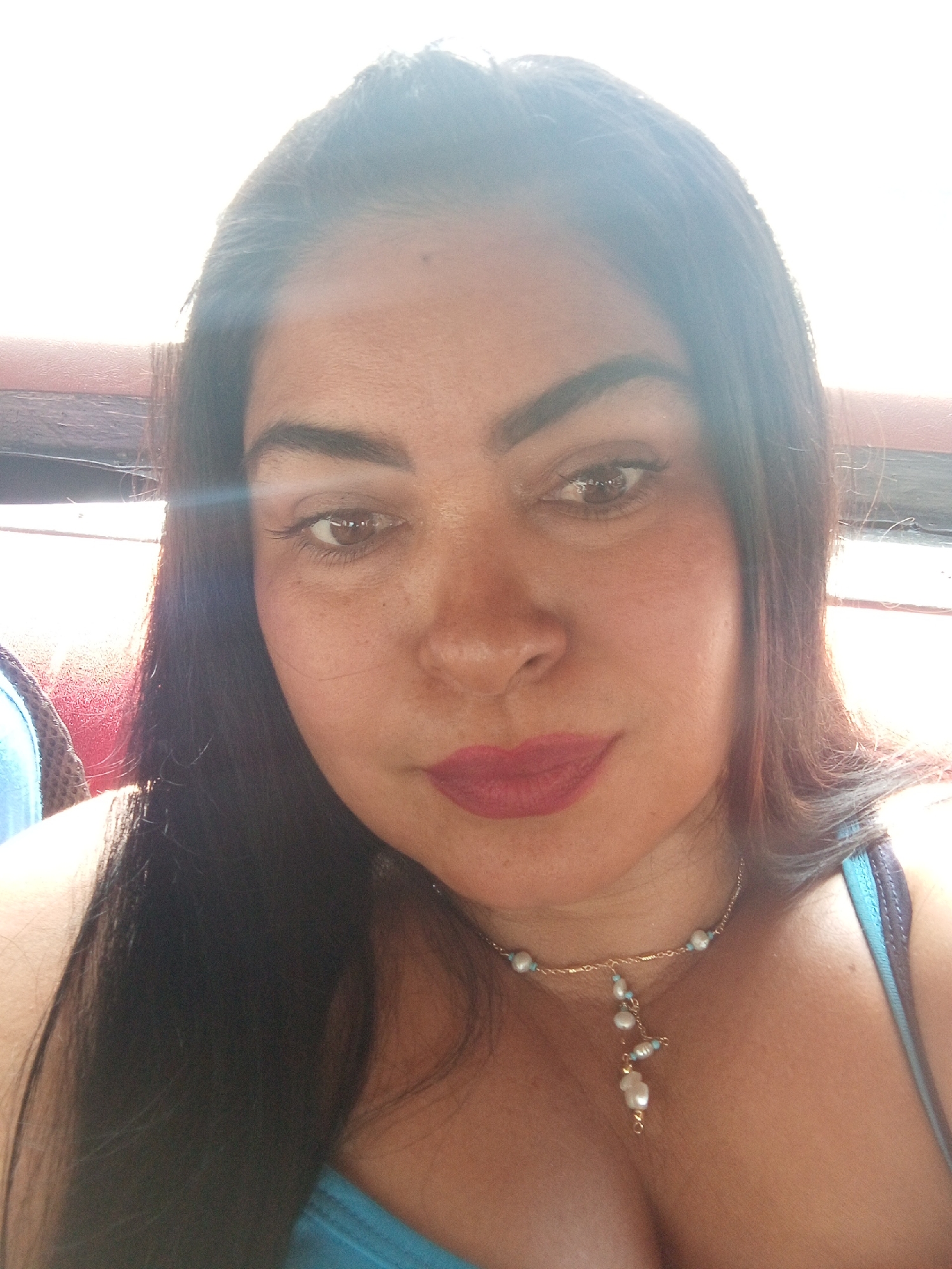 A close-up photograph depicts a woman with dark hair and brown eyes. She is wearing a blue top and a delicate gold necklace with pearls. The lighting suggests an outdoor setting. While the location is mentioned as Juan Griego, Venezuela, there are no visible environmental cues in the image to confirm or elaborate on the specific location within the city.