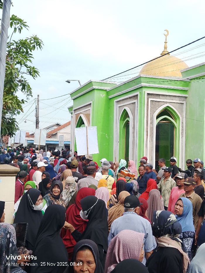 A crowd of people congregates outside a green mosque with a golden dome. Most wear head coverings. Some people hold white banners. The photo is dated "25 Nov 2025".