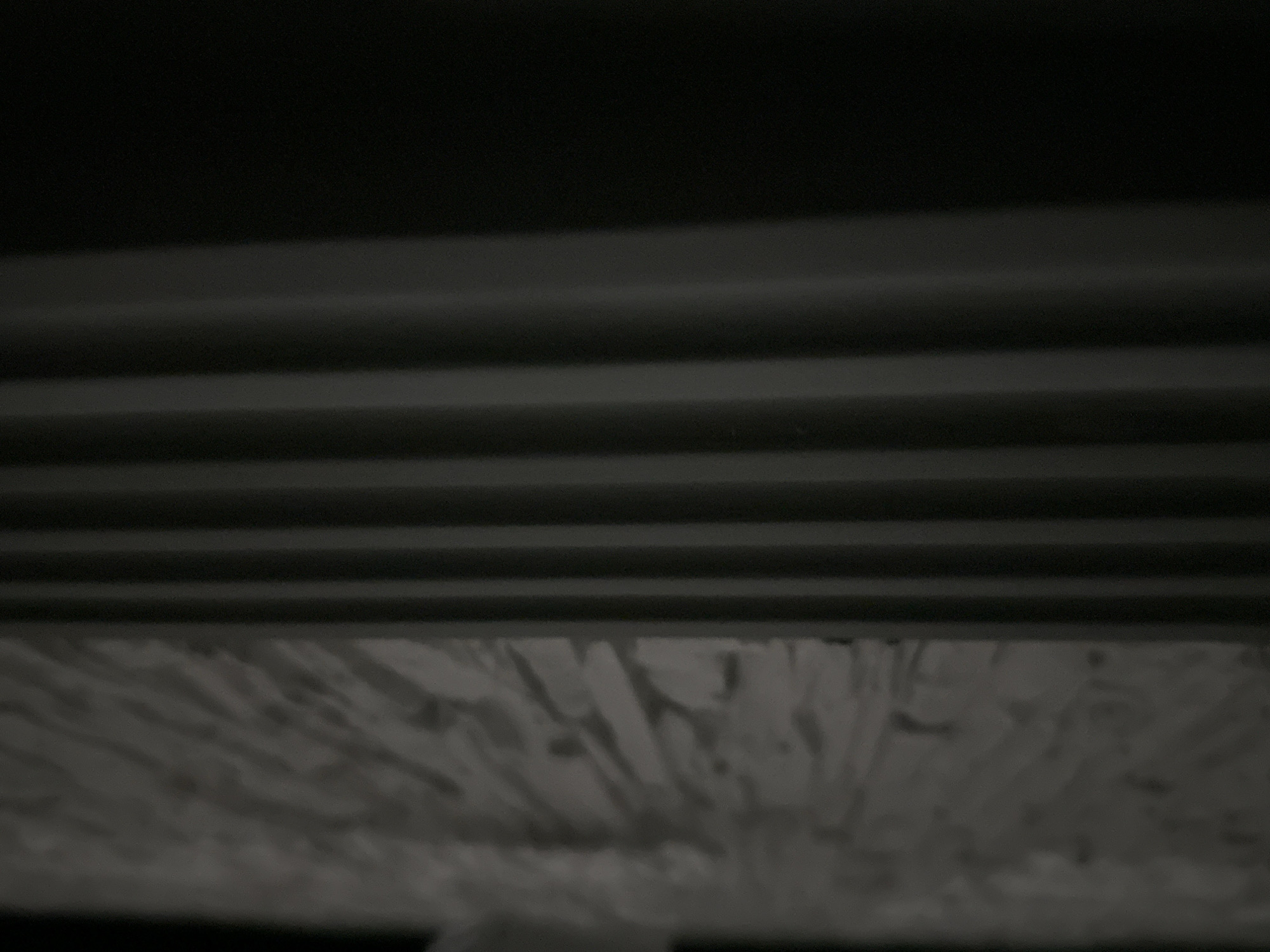 The image depicts a dark scene with a combination of linear and textured elements. In the upper portion of the frame, there are several parallel, horizontal lines, likely part of a structure. Below these lines, there is a field of rough, textured material that appears somewhat fragmented. No individuals, specific objects, actions, or interactions are discernible in the image. The environment is dark and the location details (city, state) are unknown.