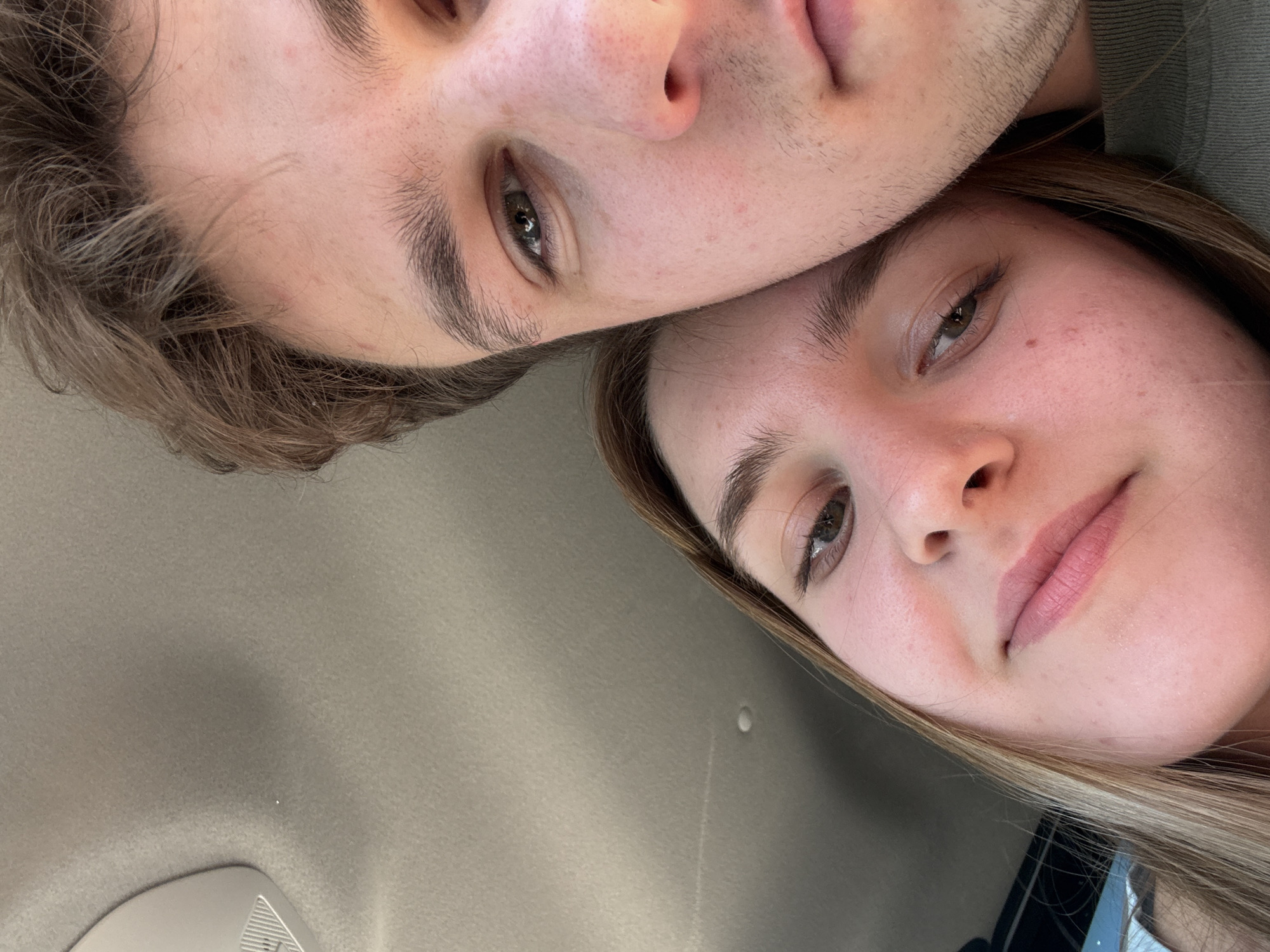 The image depicts two individuals, a male and a female, in a close-up, tilted view. The male is positioned above the female, their faces touching. The male has short, brown hair and stubble. The female has longer, blonde hair. The background appears to be the interior of a car, possibly the ceiling. The location cannot be determined to be Perm, Russia based on visual cues in the image.