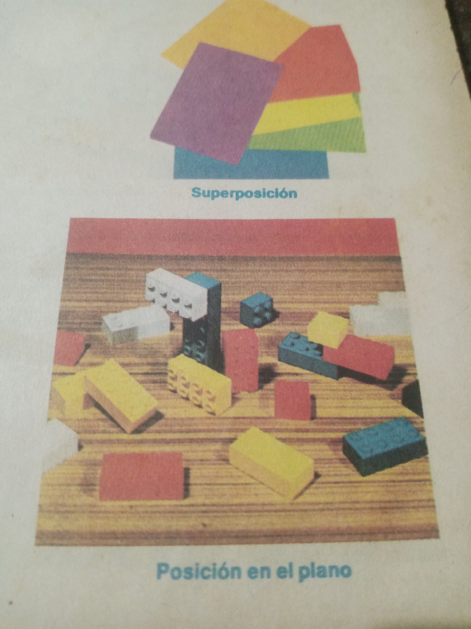 The image displays two distinct visual examples. The upper portion features a collection of colored rectangles, possibly paper or cardstock, arranged in a layered, overlapping fashion, illustrating "Superposición" (Superposition). Below this, a wooden surface is populated with various building blocks in different colors and shapes, demonstrating "Posición en el plano" (Position on the plane). The blocks include red, yellow, white, and blue pieces. The scene is a static display, likely from an educational resource. There is no indication of Santa Ana, Venezuela, or any elements that would place it in a specific city.
