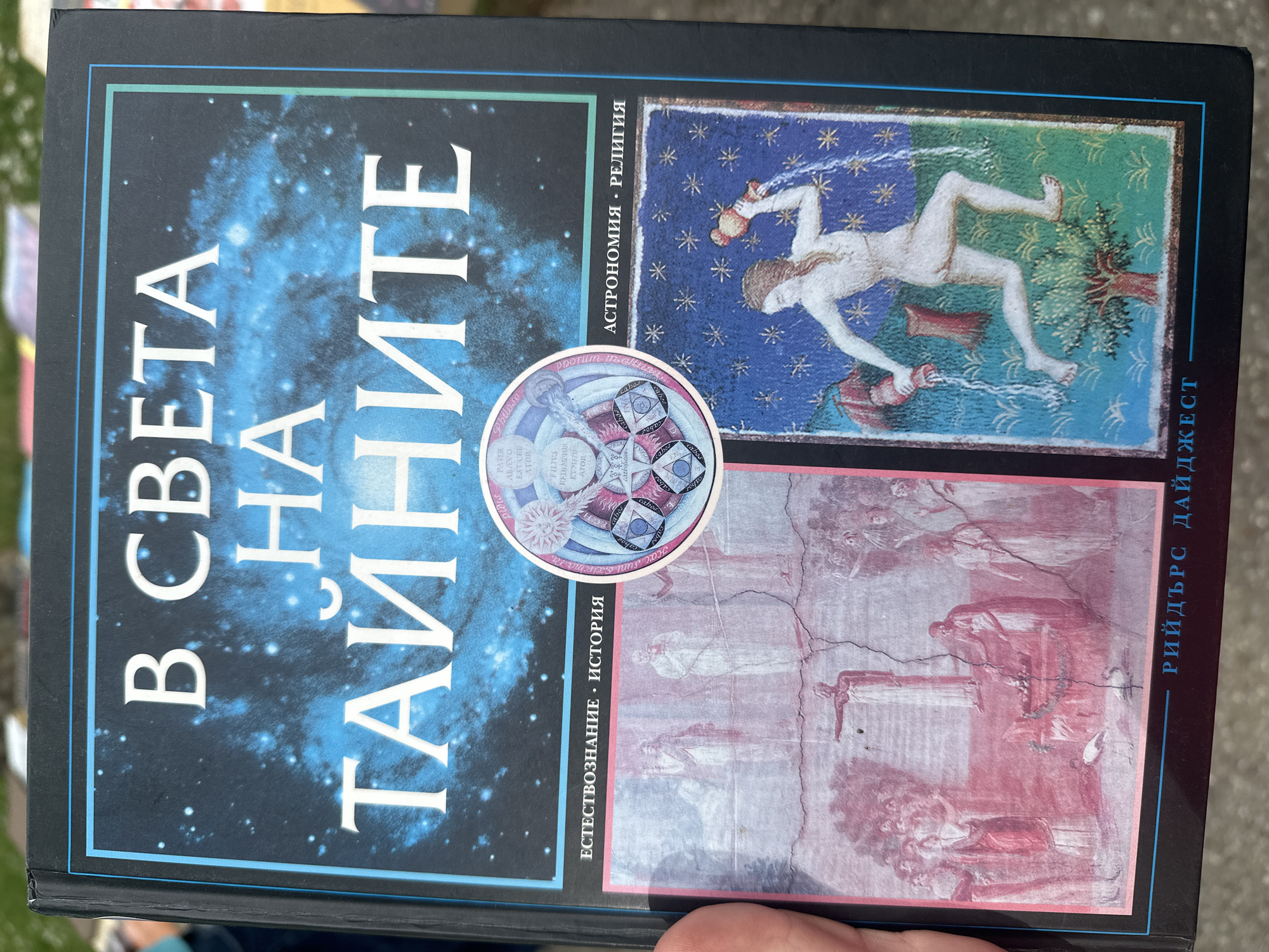 The image shows a book cover with the title "В СВЕТА НА ТАЙНИТЕ" (In the World of Secrets) in Bulgarian. The book cover features a nebula-like background and several images including historical illustrations, religious symbols, and possibly alchemical or cosmological diagrams. The author's name, "РИЙДЪРС ДАЙДЖЕСТ" (Reader's Digest), is visible on the right side of the cover. The book appears to encompass topics related to natural science, history, astronomy, and religion. There is no evidence provided to indicate the location is Veliko Tarnovo, Bulgaria.