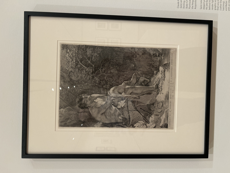 This image depicts a black-framed, matted print, identified as "Saint John the Baptist in the Wilderness" by Claude Mellan, dated 1642. The artwork, an etching and engraving, shows a partially nude male figure with curly hair, seated contemplatively in a dense, overgrown natural environment. He wears an animal skin, and a thin staff or cross is visible near his chest; his right hand supports his chin. The background features abundant foliage, trees, and a small body of water. Below the image within the print, Latin text reads "EMINENT. ET R. PRINCIPI FRANCISCO. S.R.E. CARDINALI BARBERINO" and "Claude Mellan f. 1642." The framed artwork is displayed on a plain white wall, consistent with a museum or art gallery setting. An adjacent wall-mounted informational text panel, partially visible on the right, further describes the artwork and mentions its acquisition through the "Helga and Walter Acquisition Fund." Reflections are visible on the glass covering the print. This scene is located at The Getty Center, Los Angeles, California, United States of America.