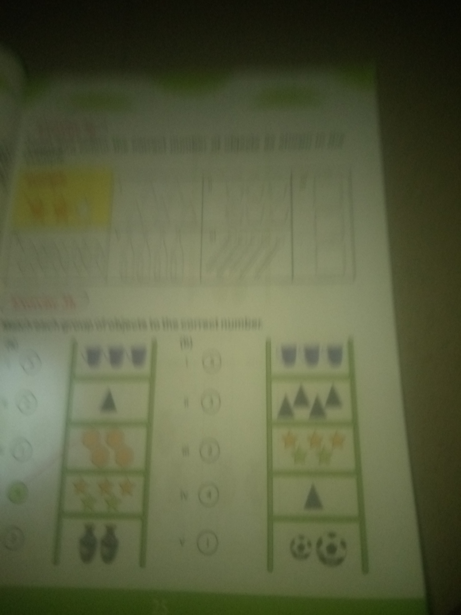 The image is a blurred photograph of a page from a children's workbook, likely for counting and matching exercises. The page is divided into sections with text and illustrations.
The top section of the page contains blurred text and line drawings of objects, possibly depicting patterns or quantities.
Below this, there is a heading "Exercise 26" followed by more blurred text: "Match each group of objects to the correct number."
The main part of the page features two vertical shelves, each containing different groups of objects arranged in rows.
The left shelf has:
- Top row: Three purple cups.
- Second row: One blue triangle.
- Third row: Four orange stars.
- Fourth row: Two blue vases.
The right shelf has:
- Top row: Five blue triangles.
- Second row: Five orange stars.
- Third row: One blue triangle.
- Fourth row: Two soccer balls.
To the left and right of the shelves are numbered circles, likely options for matching.
The image is taken from a perspective that shows a portion of a book lying flat on a surface. The lighting is dim, and the overall image quality is poor, making it difficult to read the text clearly or see fine details of the illustrations. There are no people or any context related to Jauro Yinu, Nigeria present in the image.