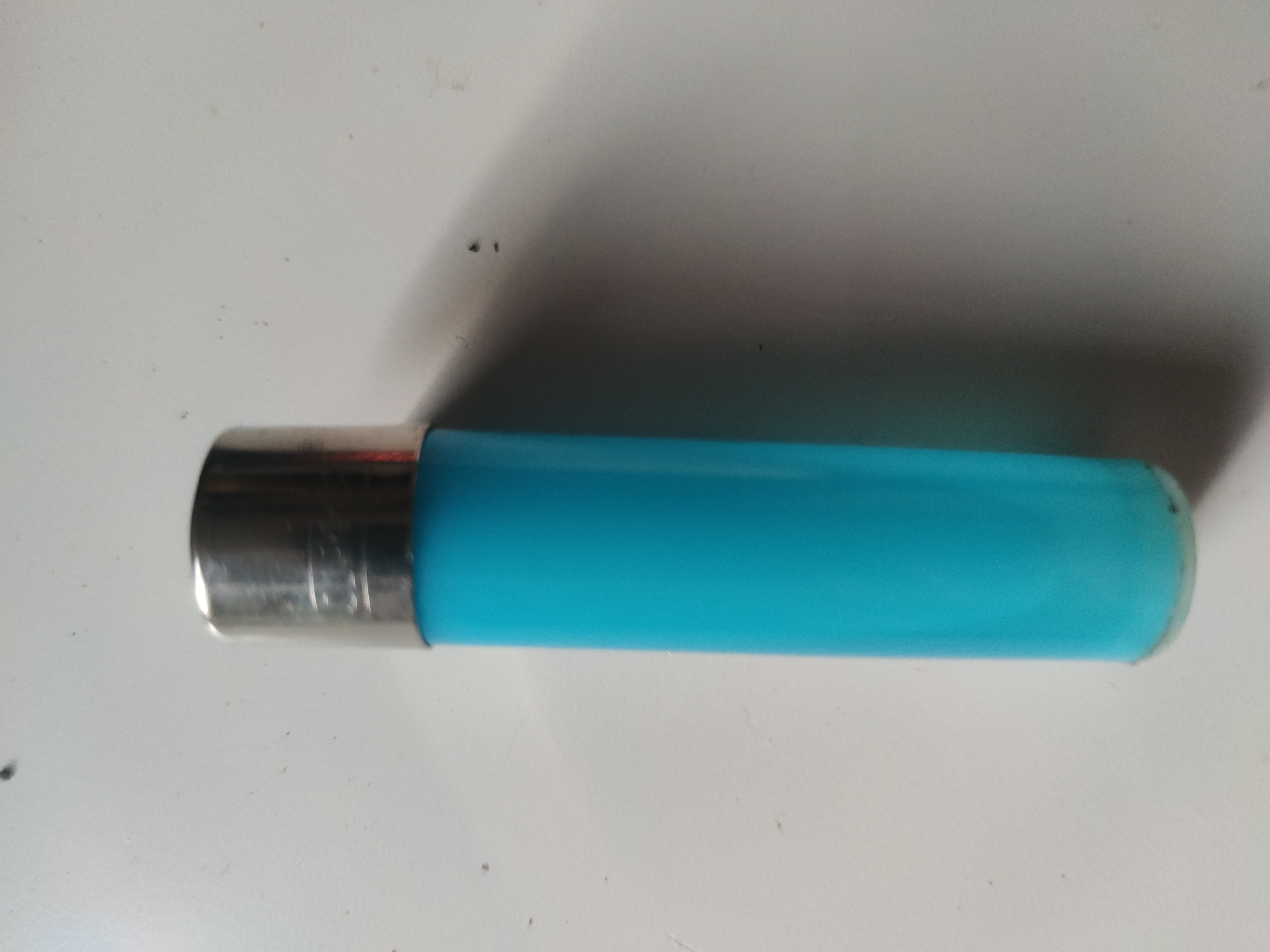 A lighter with a silver top and blue body sits on a white surface. The location is unknown.