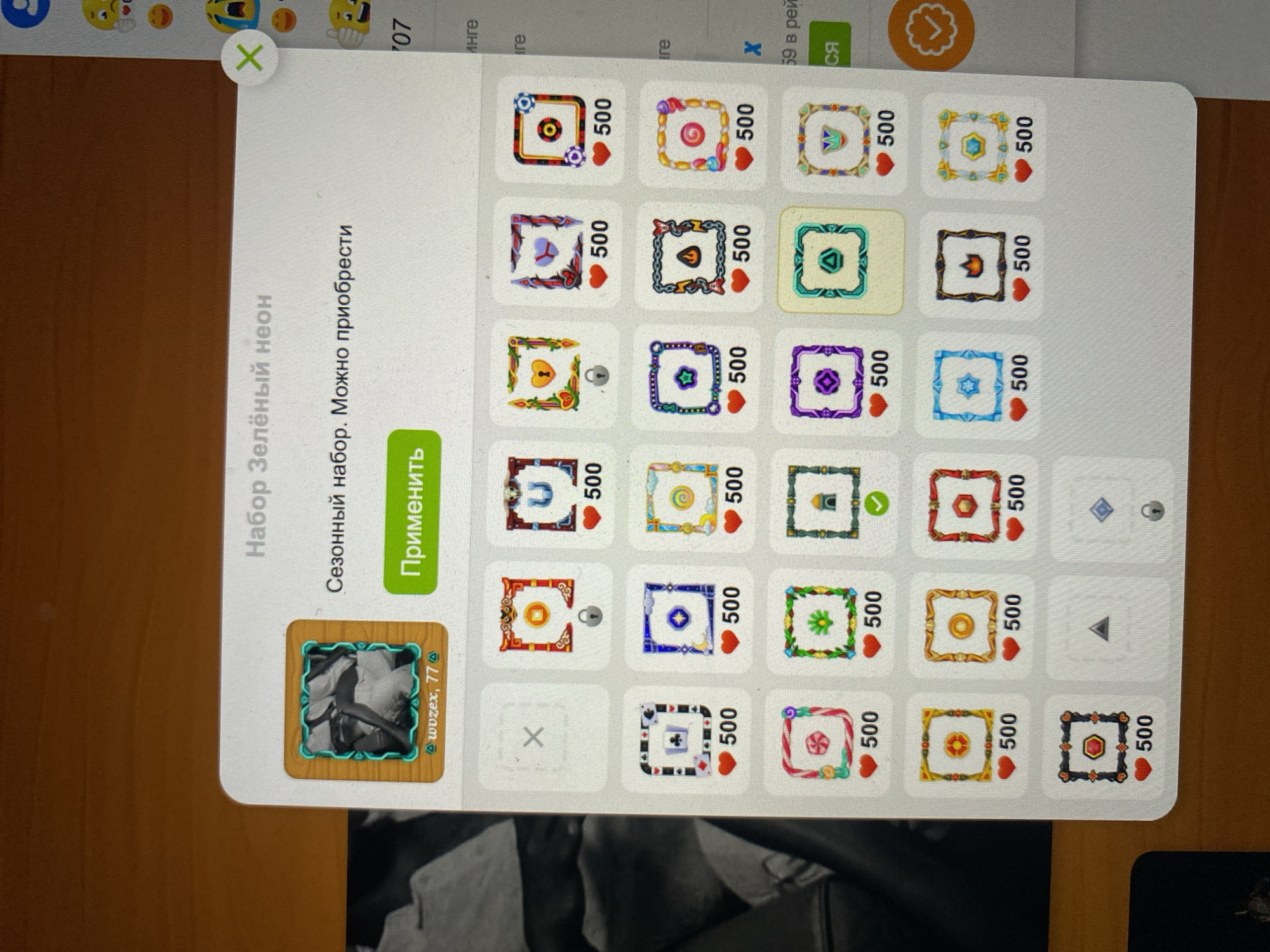 The image displays a screenshot of a user interface, likely from a mobile application or a game. The interface is primarily white with colorful icons arranged in a grid. At the top, there is a title "Набор Зелёный неон" (Green Neon Set) and a subtitle "Сезонный набор. Можно приобрести" (Seasonal Set. Can be purchased). A green button labeled "Применить" (Apply) is visible below the subtitle. To the left of these texts, there is a square icon with a wooden frame containing a black and white image of a person. Below this image, the text "wuzex, 77" is displayed along with a small icon. The rest of the interface shows a grid of smaller square icons, each featuring a decorative border and some containing a heart symbol with the number "500" below it. Some of these icons have lock symbols, indicating they are not yet available. There is also a small 'x' icon in a circle at the top right, likely for closing the interface. The background of the image is a wooden surface. There is no information in the image or the crops that relates to the city of Khankurgan, Uzbekistan.