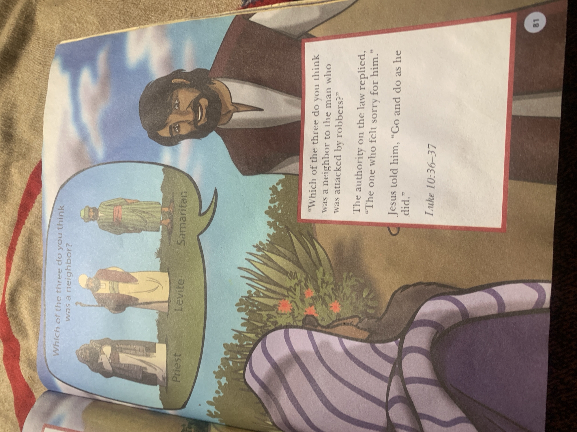 The image depicts an open book with an illustration and text. The illustration shows three figures in historical attire, labeled "Priest," "Levite," and "Samaritan," standing in a grassy area with a cloudy blue sky above. To the right, a man with dark hair and beard is shown smiling, looking towards the viewer. A portion of another person, wearing a purple and white striped garment, is visible on the left side of the illustration, facing away.
A red-bordered box on the right side contains text from a biblical passage. The text reads: "Which of the three do you think was a neighbor to the man who was attacked by robbers?" Below this, it states, "The authority on the law replied, “The one who felt sorry for him.” Jesus told him, “Go and do as he did.” Luke 10:36–37." A page number "81" is visible in the lower right corner of the book. The background suggests the book is lying on a textured surface, possibly a blanket or fabric, with a red stripe visible. There is no indication of the location being Jauro Yinu, Nigeria.