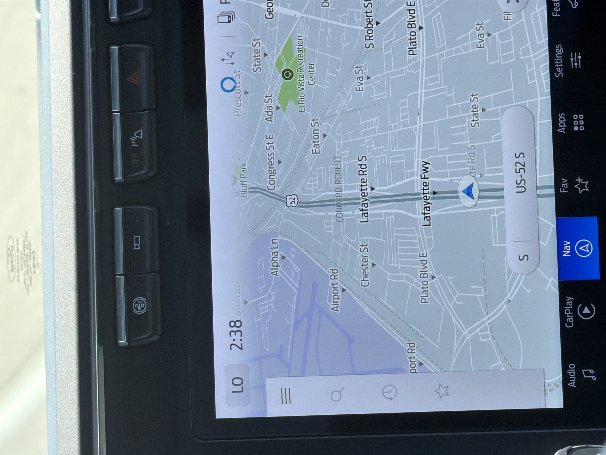The image shows a car's dashboard navigation screen. The screen displays a map with roads labeled such as "Alpha Ln", "Airport Rd", "Chester St", "Lafayette Fwy", "Plato Blvd E", and "State St". The current time displayed on the screen is 2:38. The location is identified as "El Rio Vista Recreation Center" within Saint Paul, United States of America. On the top of the screen, there are buttons for parking assist and hazard lights. Below the map, there are icons for "Audio", "CarPlay", "Nav", "Fav", "Apps", "Settings", and "Features". The vehicle is in "LO" mode, indicating a low gear setting.
