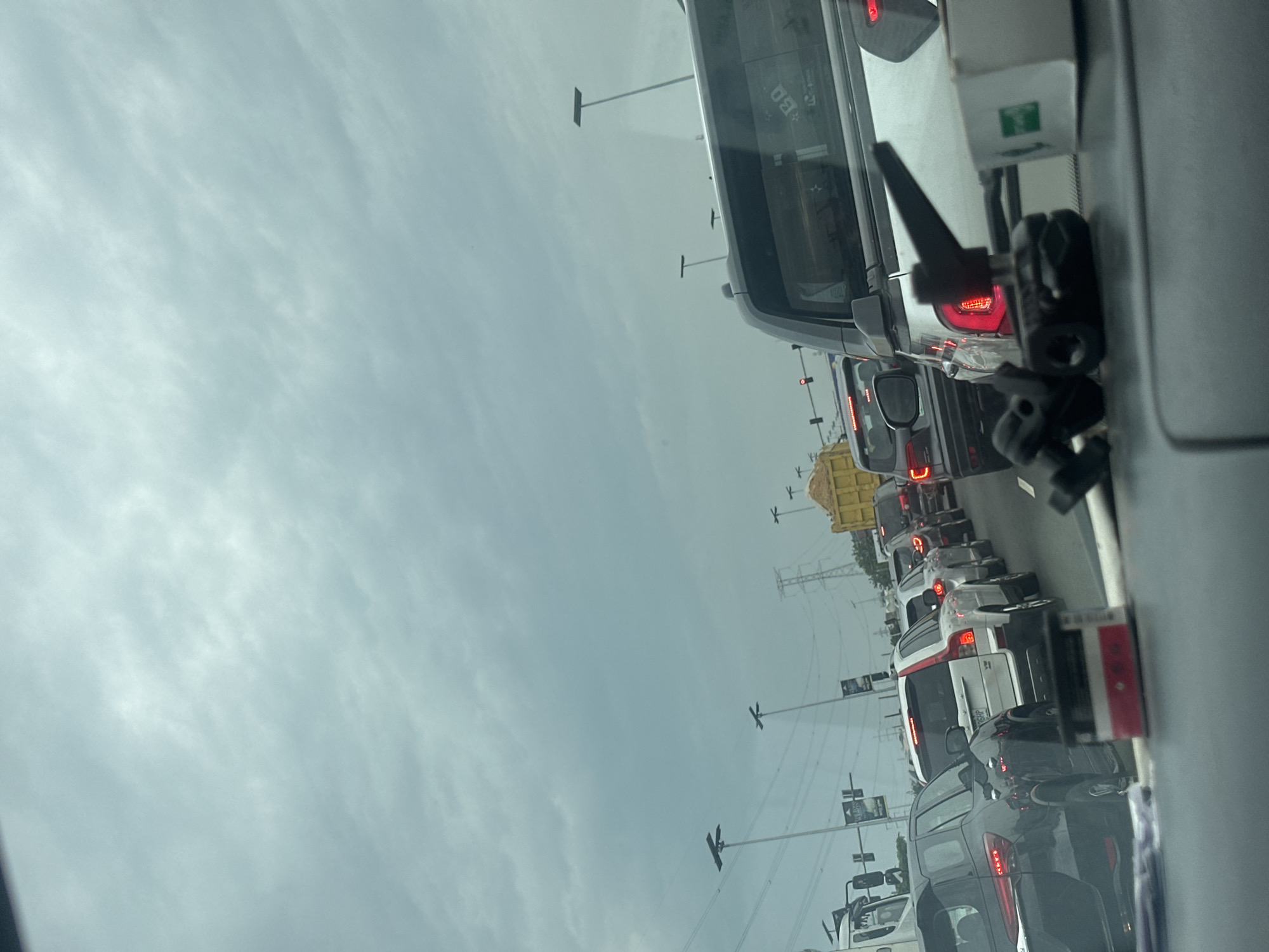 The image depicts heavy traffic congestion on a road in an urban area. The sky is overcast. Various types of vehicles are visible, including cars, trucks, and buses. Utility poles and power lines are present along the roadside. No people are visible in the frame. The city is Unknown, Unknown.
