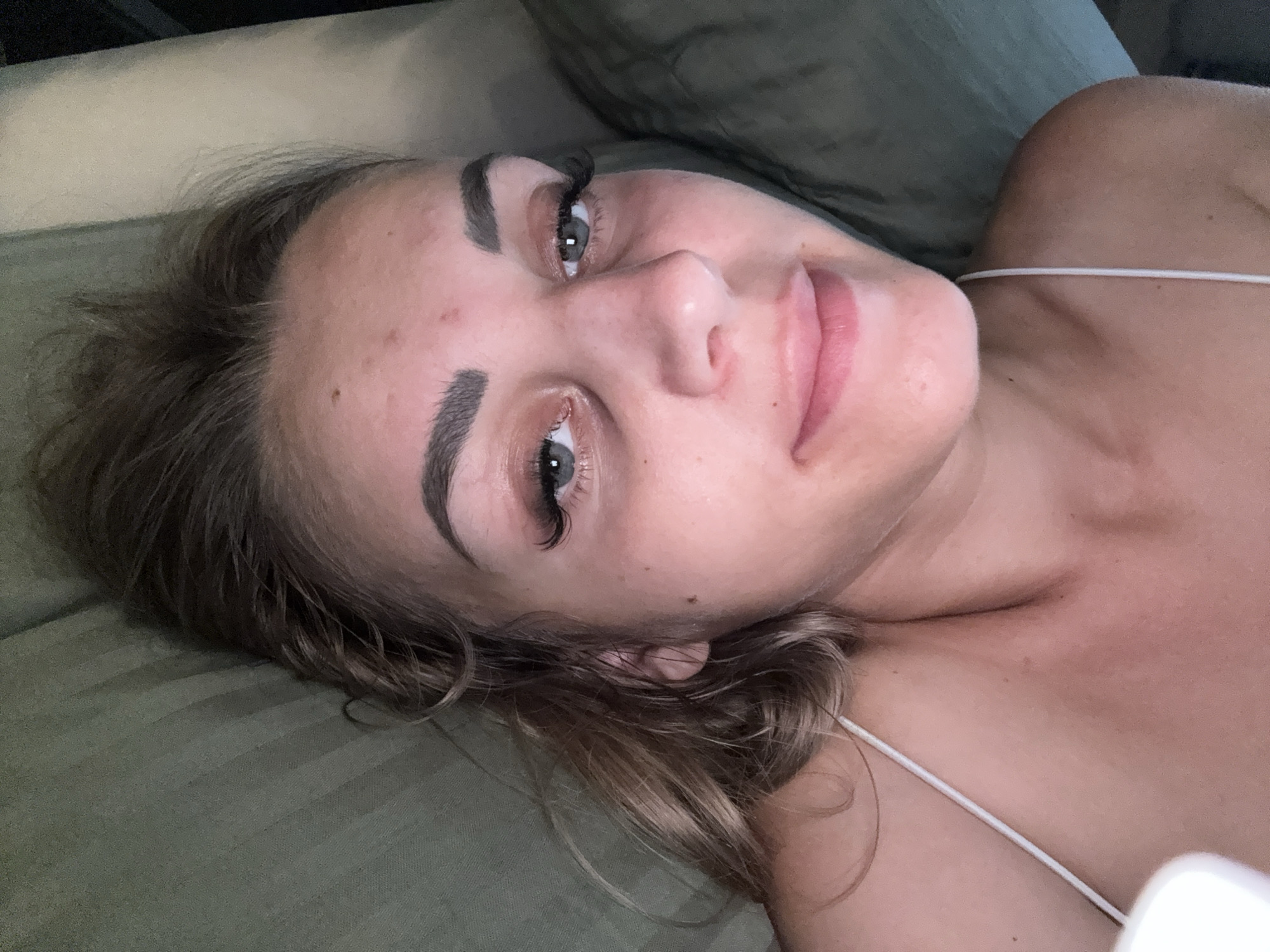 A woman with fair skin, light brown hair, and green eyes is lying down on a green surface. She is wearing a white strap. Her head is tilted to the side, and her eyes are open. The background appears to be a couch or bed. There is no visible information that would allow for the identification of the specific location in Yuzhno-Sakhalinsk, Russia.