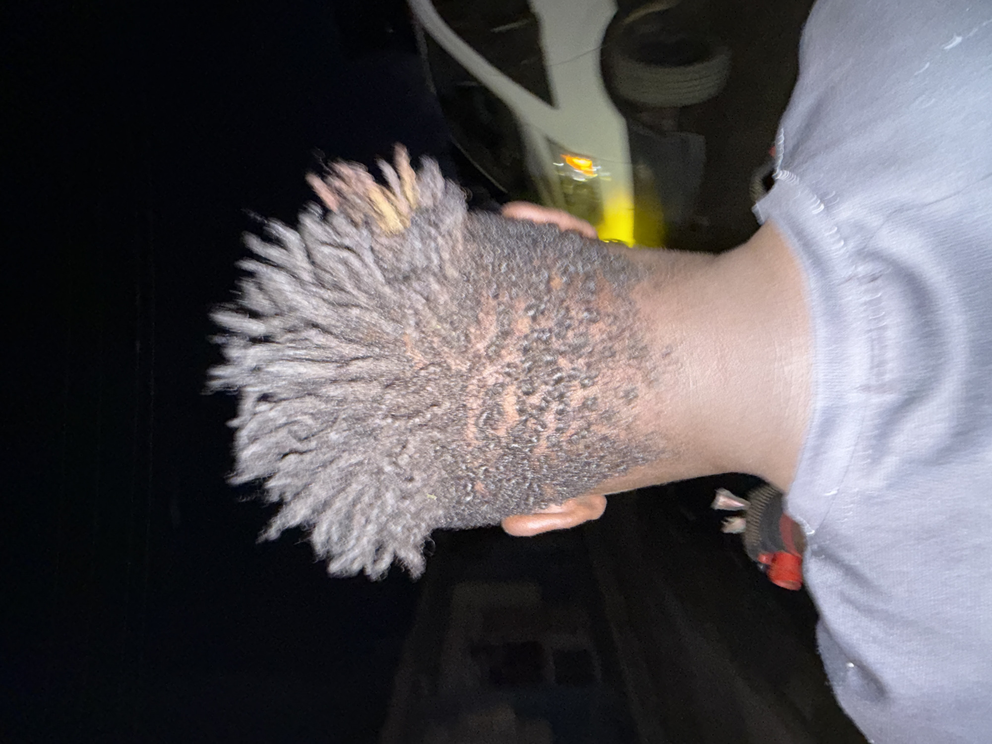 The image shows a man with short dreadlocks, possibly standing next to a vehicle. The environment is dark, but there is some light reflecting off the car. It is impossible to confirm the location or any details about Lekki, Nigeria from the available information.