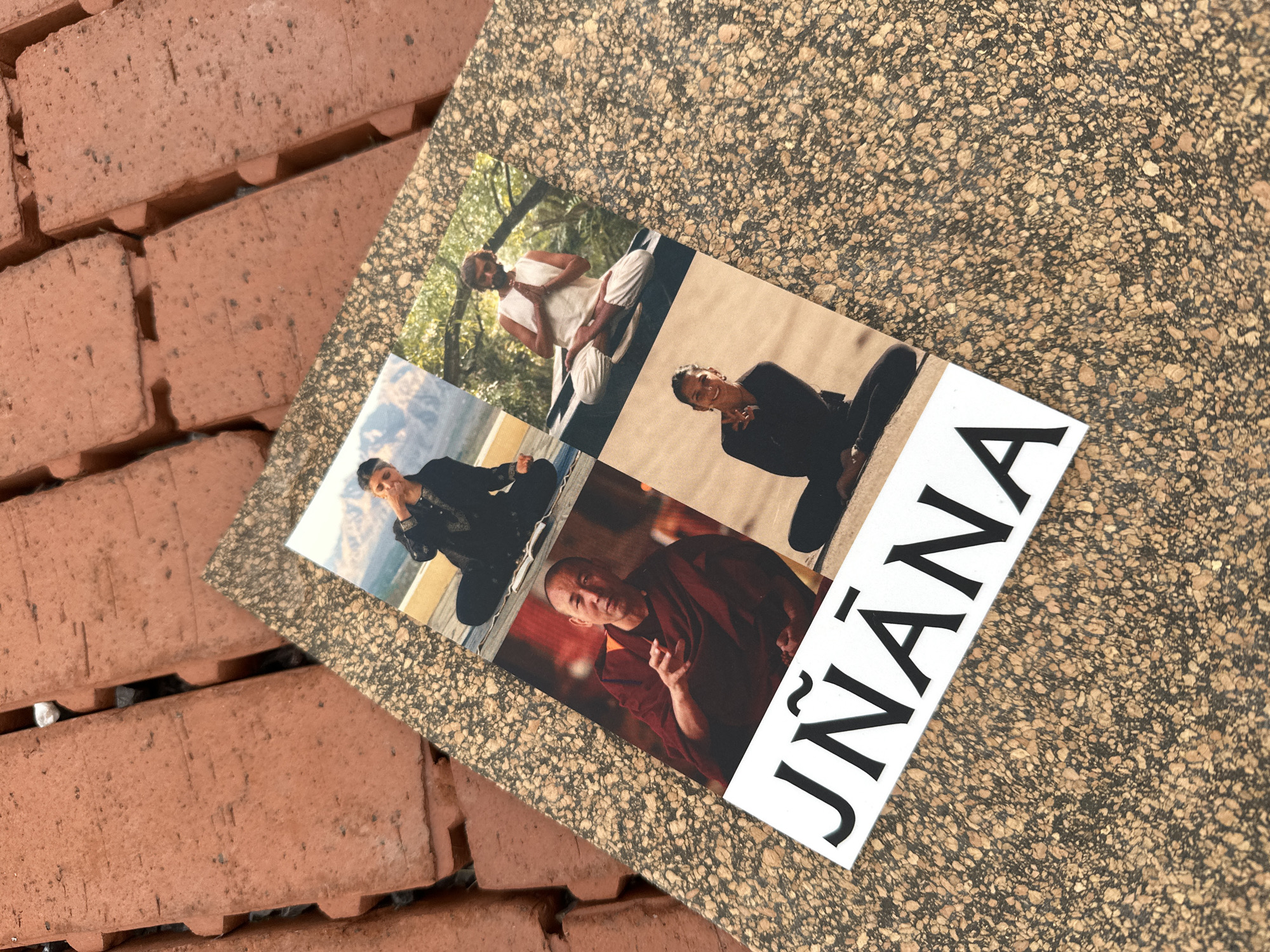 Four photos are arranged in a collage on a speckled, cork-like surface, which rests on a reddish-brown brick surface. The collage features individuals meditating. The top left photo shows a person in a black outfit with their eyes closed and hands on their chest. The top right photo displays a person in white attire, with their hands in a prayer position. The bottom left photo features a man in a maroon robe, with his hands gesturing. The bottom right photo shows a person in a black outfit, also meditating. Below the collage, the word "JNĀNA" is printed in large, black, capital letters on a white background. The brick surface suggests an outdoor setting, possibly a pathway or patio. The image does not provide any specific location in London.