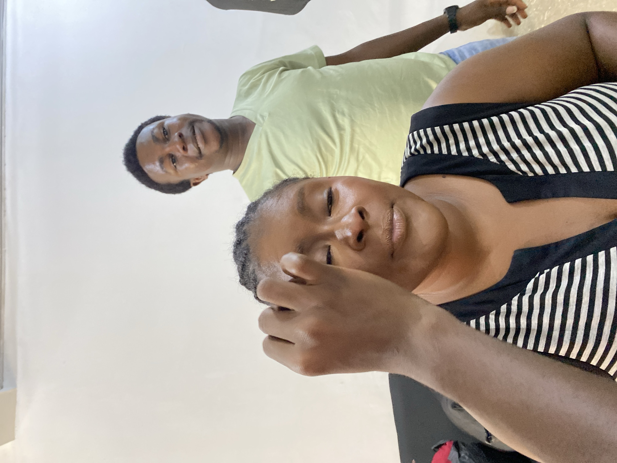 Two individuals are visible. One is wearing a light yellow shirt, and the other is wearing a black and white striped top. The setting appears to be indoors with a plain wall in the background. The photograph was taken from a high angle, looking down at the subjects. The location provided is Gura Top, Nigeria.