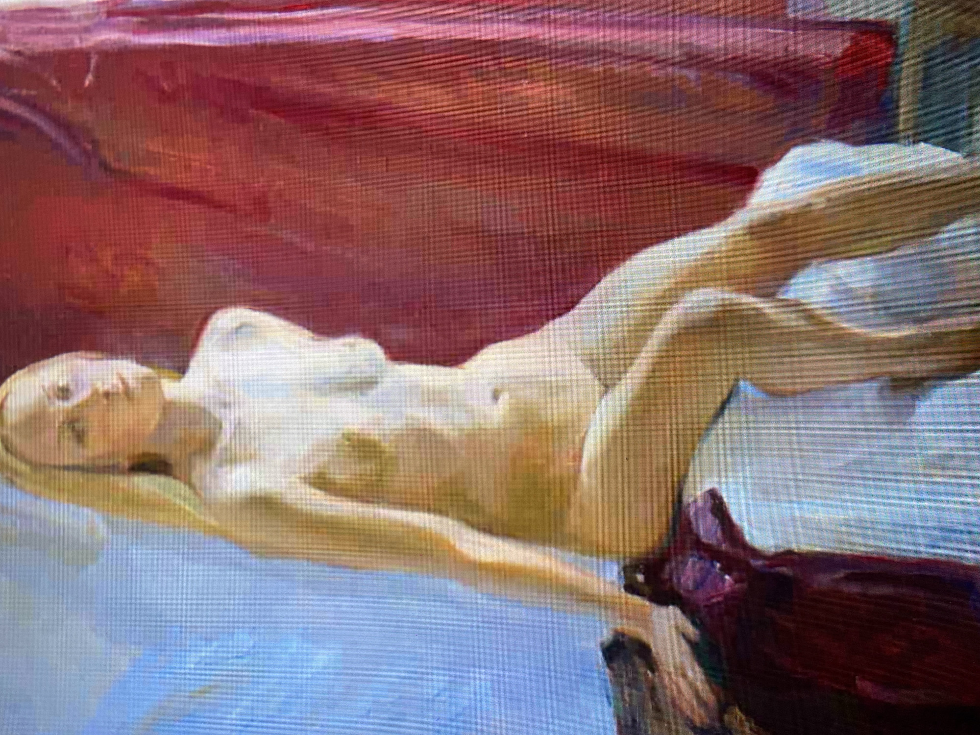 A painting depicts a nude woman with blonde hair sitting on a white cloth. She is looking to her right, with her left arm resting on her leg and her right arm bent at the elbow. She is wearing a dark red fabric draped over her left side. In the background, a red curtain is visible. The lighting suggests a studio setting.