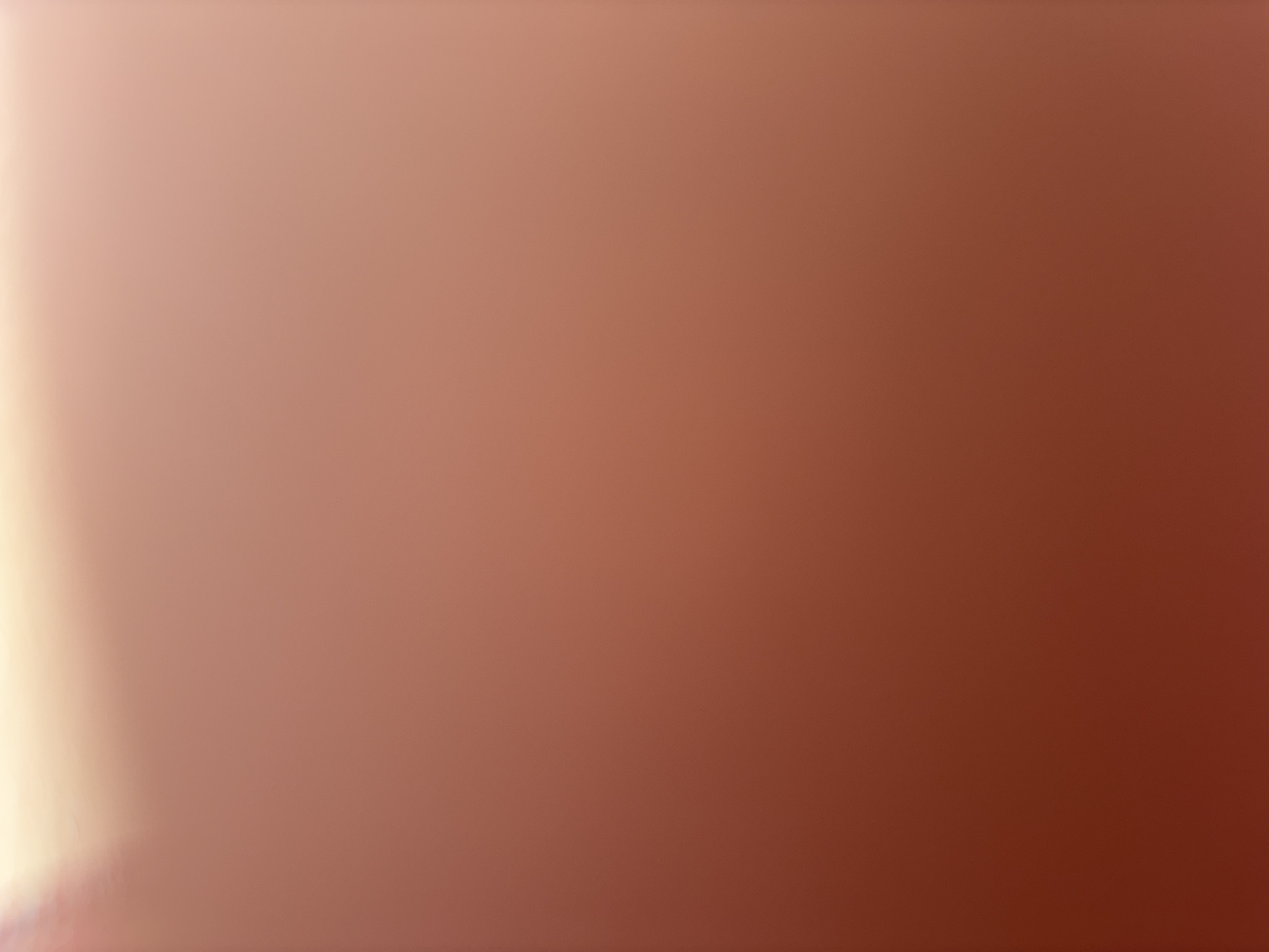 The image shows a blurry gradient of color shifting from a light beige/tan on the left to a darker reddish-brown on the right. There are no discernible objects, people, or locations visible in the image.