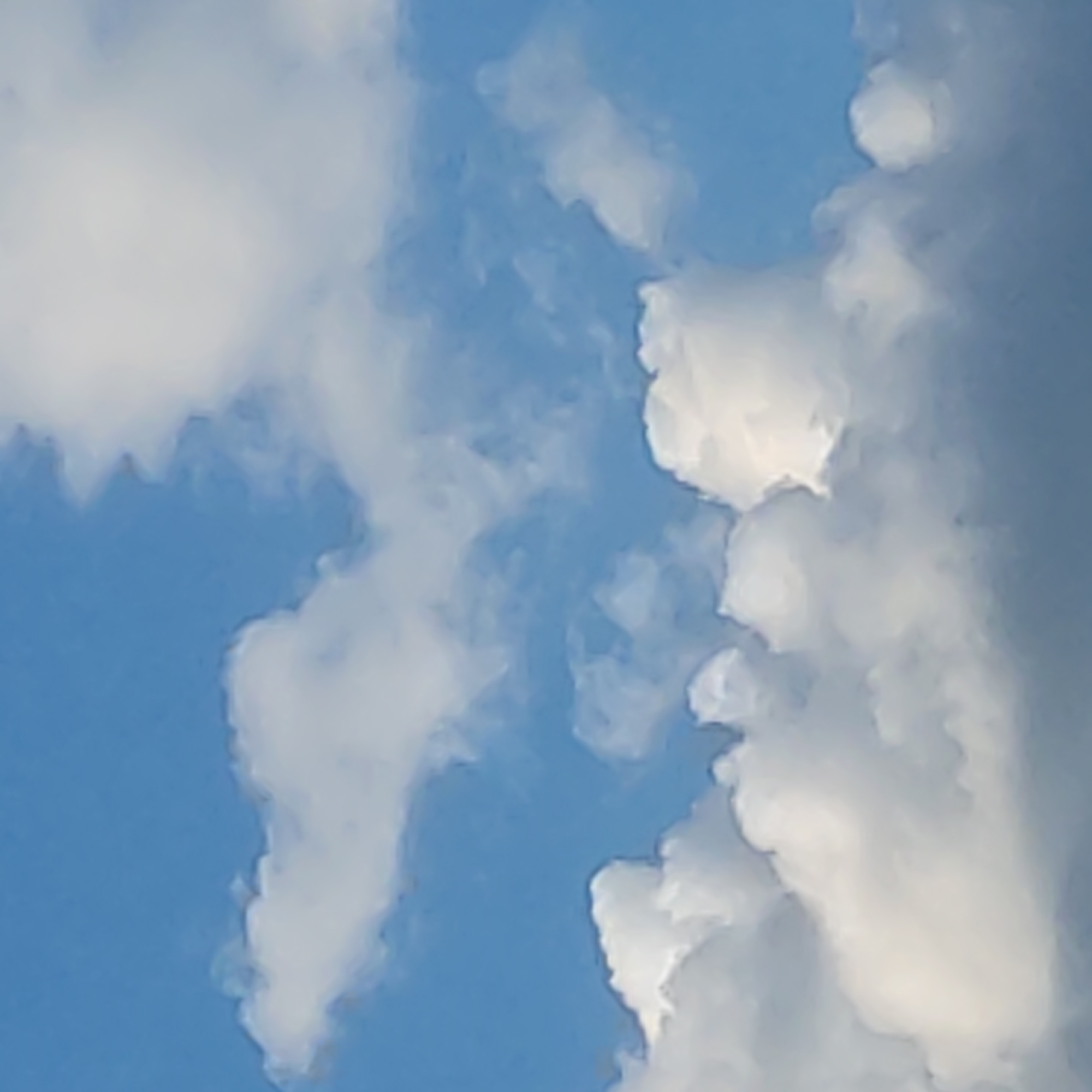 The image is an outdoor, eye-level, close-up shot of a blue sky with scattered white clouds. The clouds are fluffy and billowy, with some appearing brighter and more defined than others. The lighting suggests it is daytime, likely with sunlight filtering through the clouds, creating areas of shadow and highlight. There are no people, structures, or identifiable landmarks visible in the image. The scene is an unobstructed view of the sky.