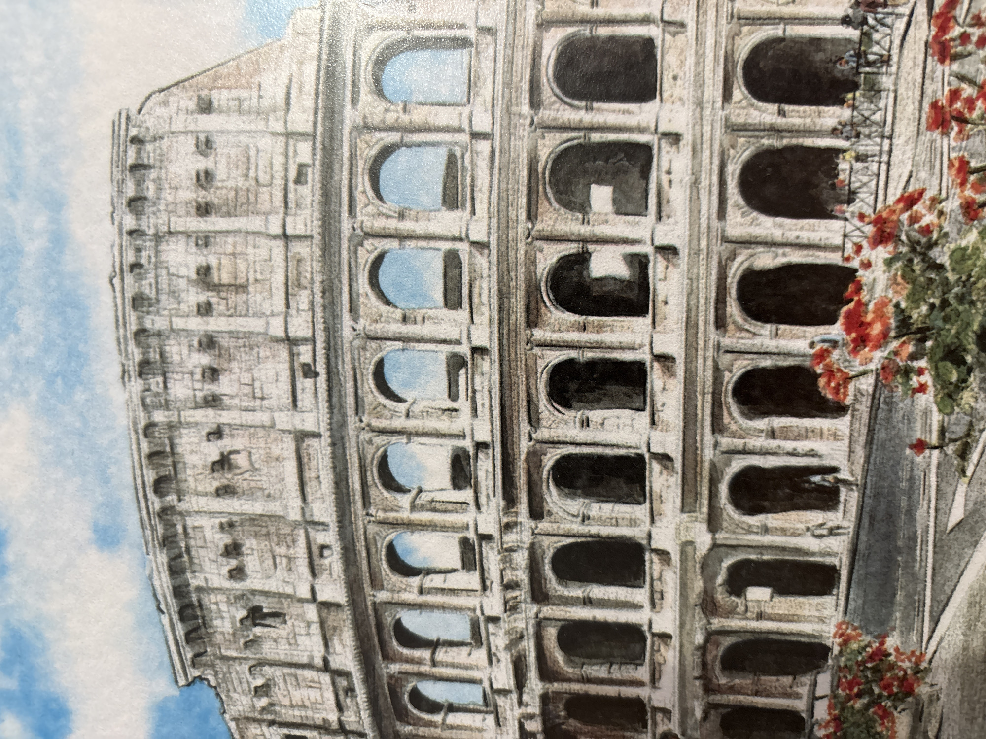 The image is a watercolor painting of the Colosseum in Rome, Italy. The ancient amphitheater is depicted with its characteristic arches and weathered stone facade under a blue sky with white clouds. The foreground features a street leading up to the structure, with a railing and several small figures of people standing and walking. Red flowers are blooming in pots and along the edge of the street. The painting captures the grandeur of the historic monument.