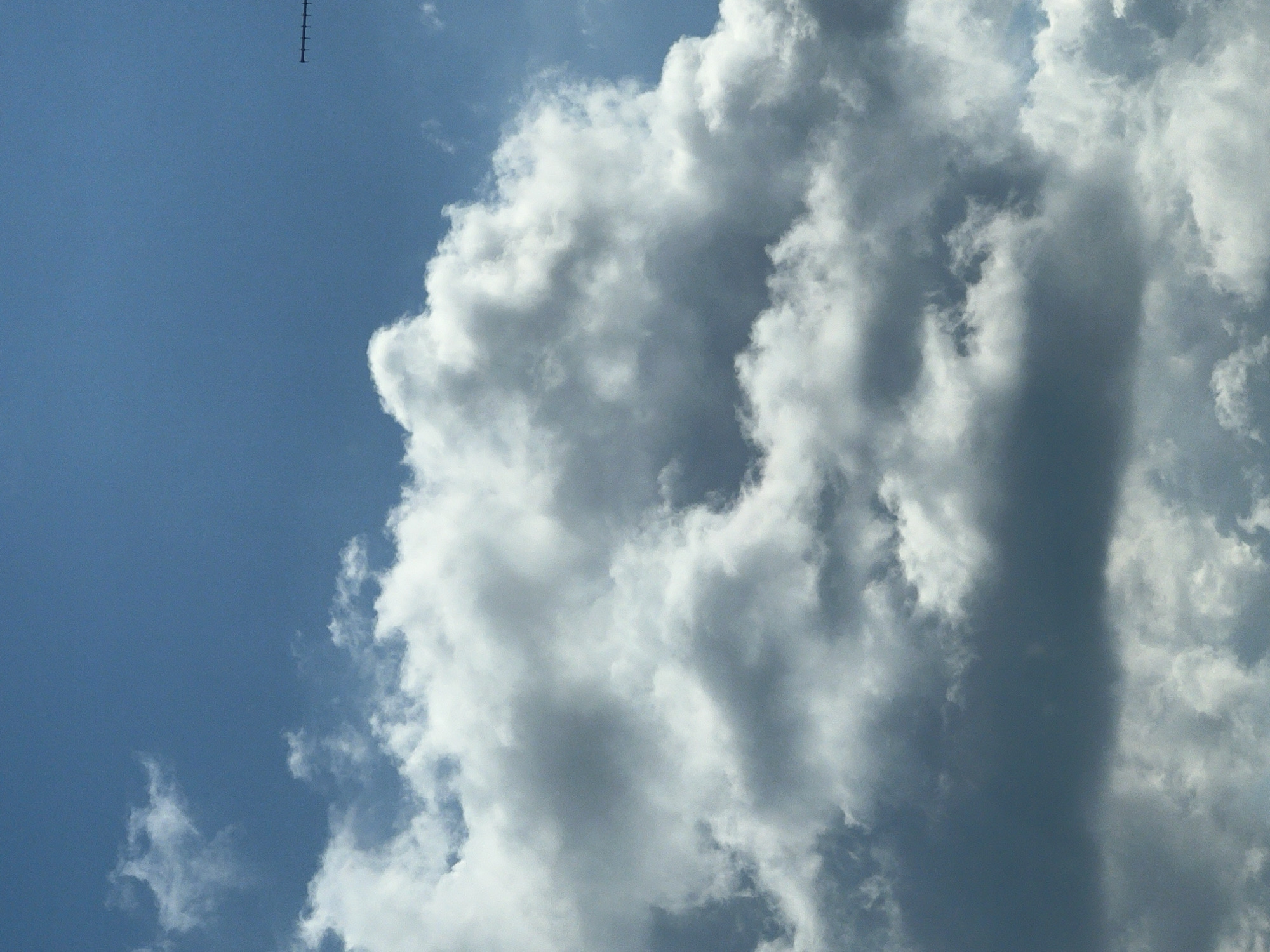 The image shows a cloudy sky. In the upper right corner, a black object resembling an antenna or a mast is visible against the blue sky and clouds. There are no people or identifiable landmarks of Warsaw, Poland present in the image.