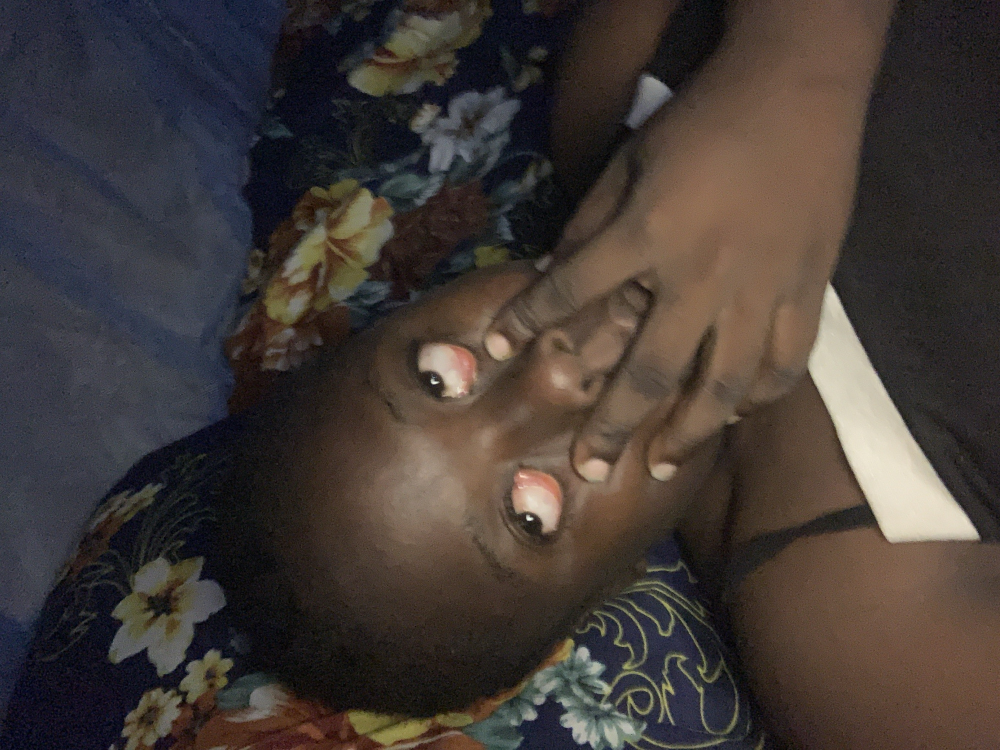 A dark-skinned person with bloodshot eyes is lying down, partially obscured by a floral patterned fabric. The person's hand is near their face. The location is not discernable as Kukum, Nigeria, or any other specific place, from the details present in the image.