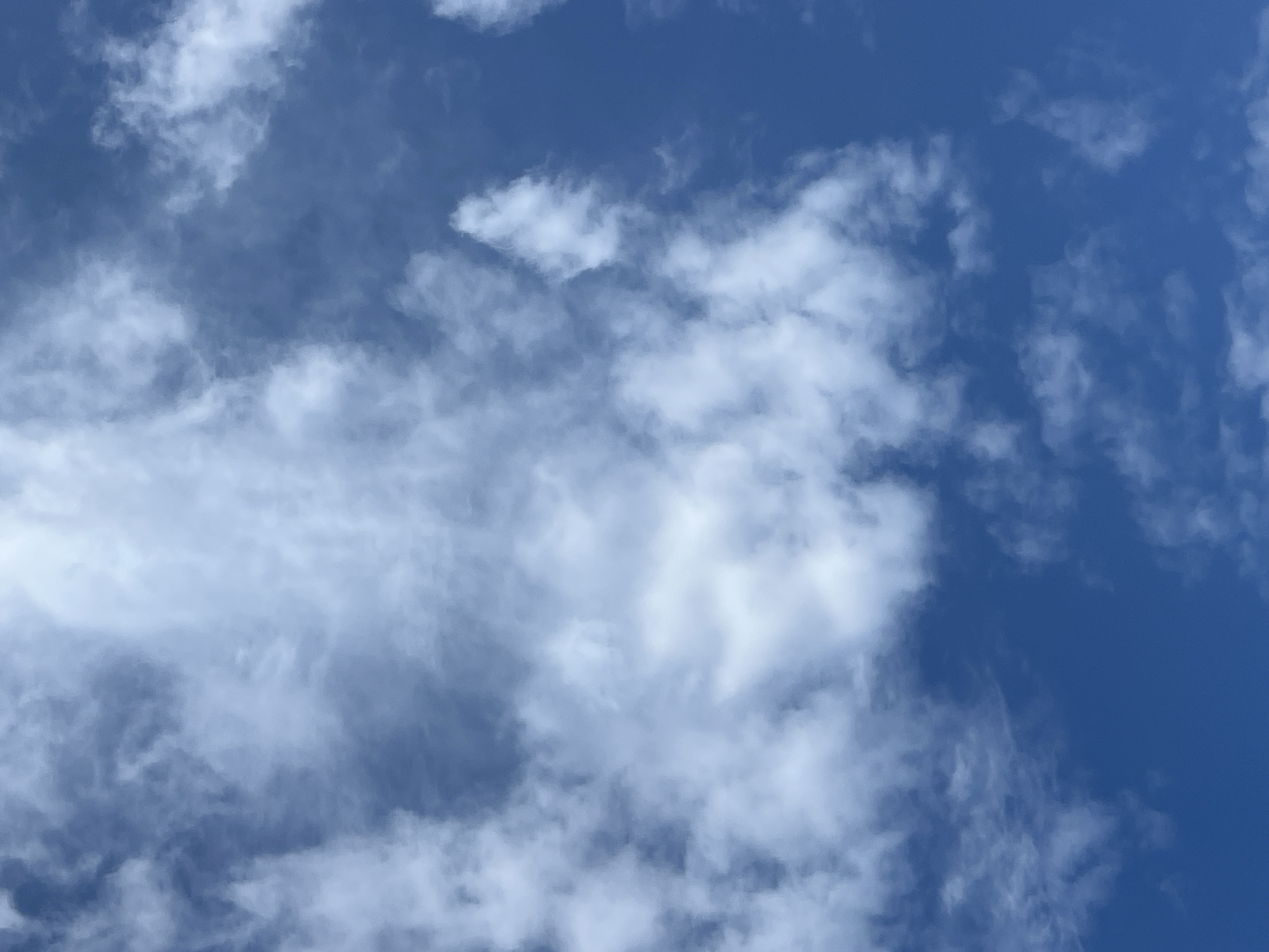 This media file depicts a sky with scattered clouds against a deep blue background. The clouds are predominantly white and wispy, with some appearing denser and more substantial than others. They are illuminated from above, suggesting it is daytime. The overall impression is of a pleasant, possibly breezy day, with the clouds adding texture and visual interest to the expanse of blue. There are no people or objects visible, and no text is present in the image. The setting is an outdoor scene focused solely on the sky.