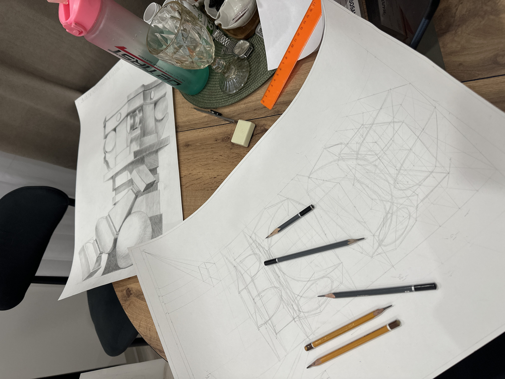 This image depicts a work area on a wooden surface with drawing materials. There are two sheets of paper. One contains a shaded pencil drawing of geometric forms and the other contains a perspective drawing with numerous construction lines. Lying on the drawing are several pencils, an eraser, and an orange ruler. Also present are a drinking bottle, some glass vessels, and a mat.
There's no discernible information to specify a location within Kazan, Russia. The details of the image are limited to the drawing materials and the immediate surrounding objects. There are no identifiable elements that indicate geographical location or the presence of any people.