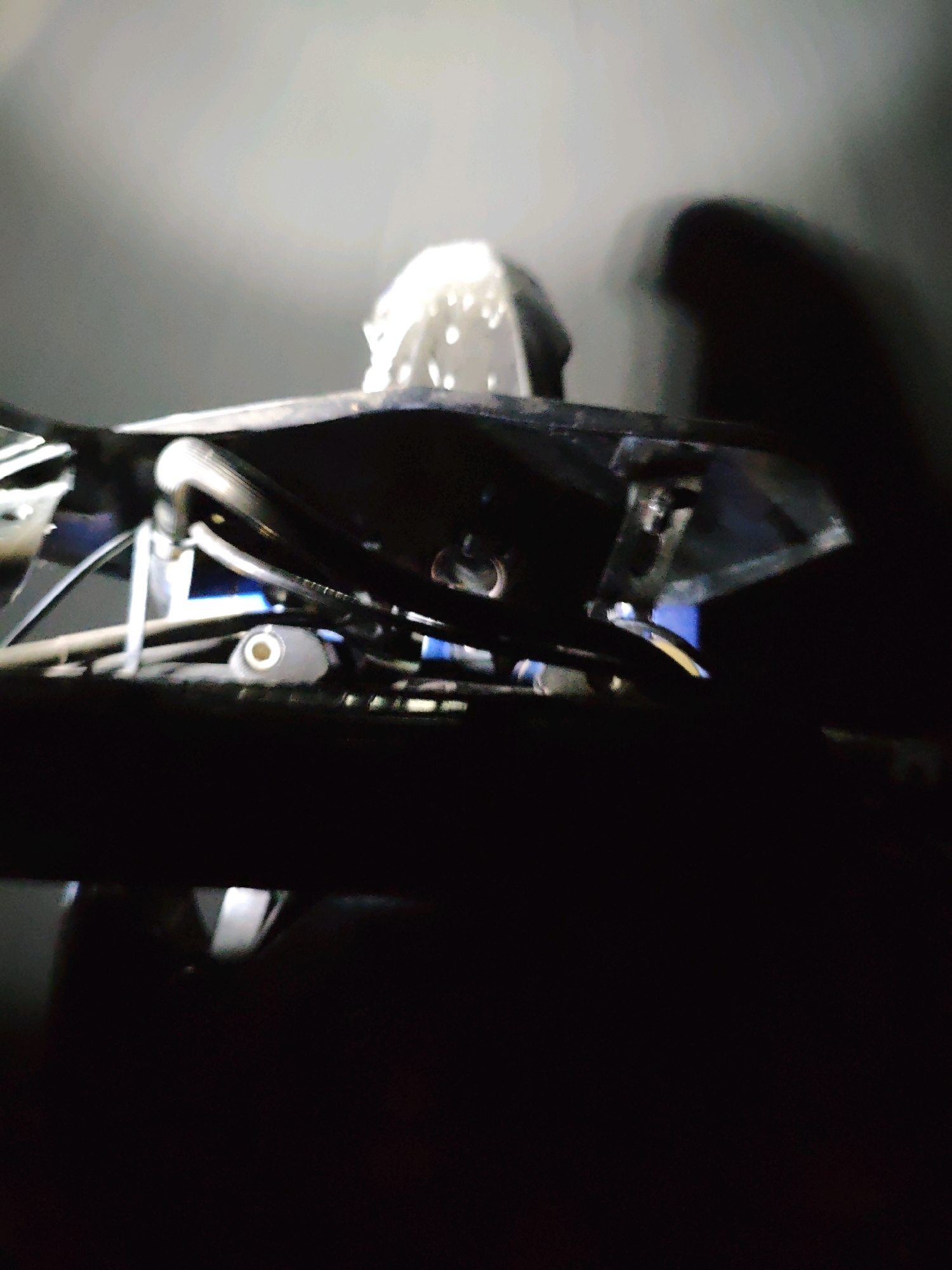 The image shows a dimly lit, abstract view of what appears to be part of a vehicle or machinery. The focus is on metal components and hoses, with a bright light source creating a halo effect and a dark, blurred background. There are no discernible people, animals, or clear geographical markers to indicate a specific location. The scene is devoid of any identifiable context related to the city of Penantian, Indonesia.