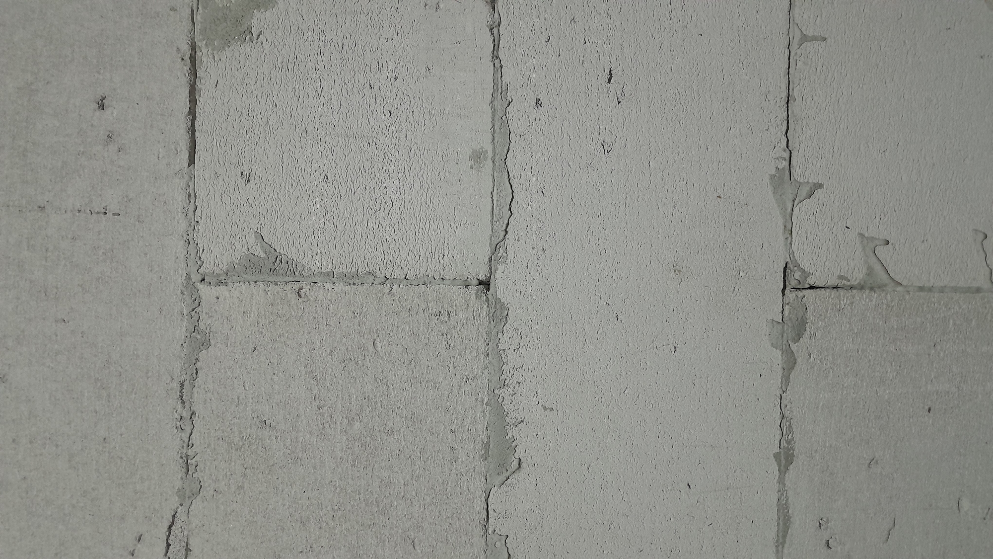 The image displays a close-up, straight-on view of a wall constructed from pale gray concrete blocks. The blocks are laid horizontally, with visible mortar lines between them. The texture of the blocks is rough and porous, with some areas exhibiting a slightly smoother finish. There are subtle variations in the tone of the gray, with some blocks appearing lighter or darker than others.
The wall appears to be in a state of construction or disrepair. Uneven application of mortar is evident, with some areas showing drips and irregular edges where the mortar has not been fully smoothed. The surface of the blocks also shows signs of wear and imperfections, such as small pits and possibly some surface chips.
The lighting is flat and diffused, suggesting an overcast day or an indoor setting without direct light sources. The overall impression is one of a utilitarian and unadorned structure. There are no people or other discernible objects visible in the frame, focusing solely on the texture and construction of the wall.
This scene could be located in Sumberarum, Indonesia, as part of a building under construction, a newly finished structure awaiting finishing touches, or an older wall exhibiting signs of weathering and age. The materials and construction method are common in many regions, including Indonesia.