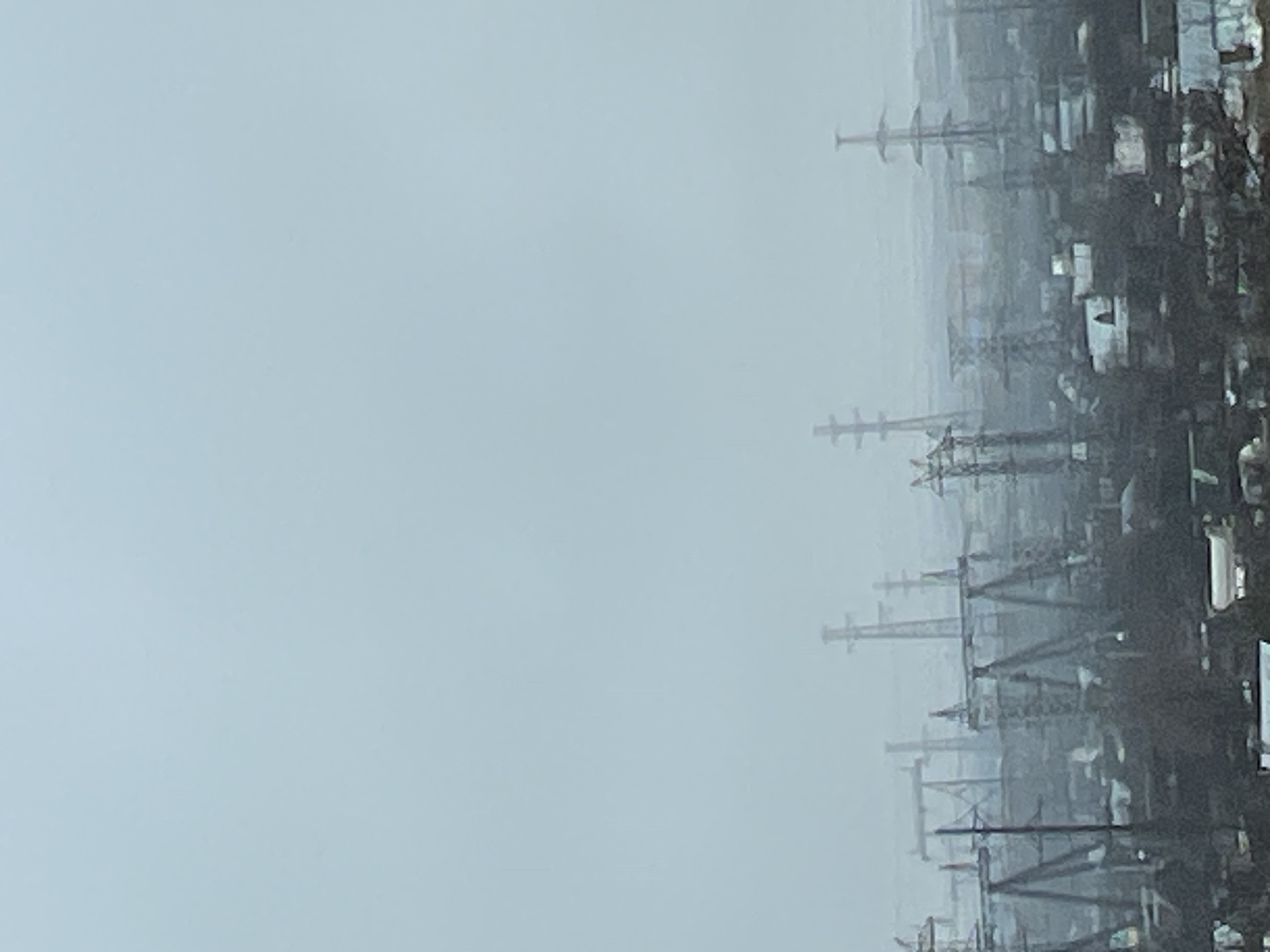 The image presents a view within the city of Chaikovsky, Russia, characterized by a heavy overcast sky. Power lines and supporting infrastructure are visible against the background.