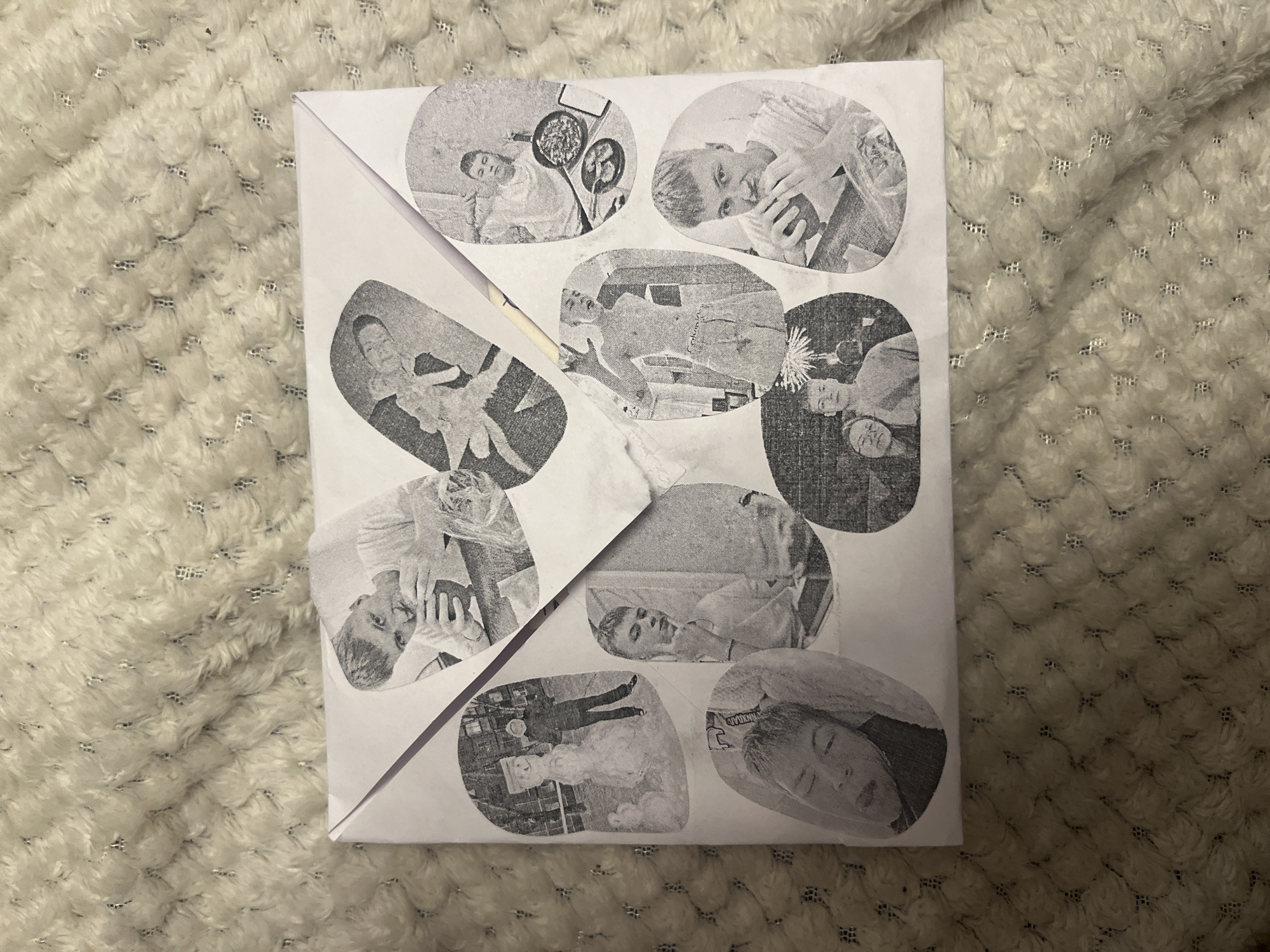 The image shows a white envelope covered in a collage of circular black and white photographs. The envelope is placed on a fluffy, cream-colored blanket. There are at least nine photographs visible, each featuring a young man. Some photos show him with friends or family, while others feature him alone in various settings, such as outdoors with a snowman, indoors with food, or posing shirtless. The photographs are adhered to the envelope in a scattered pattern. The lighting is dim, and the focus is on the envelope and its photographic adornments. The context of Svietlahorsk, Belarus is not discernible from the image itself.