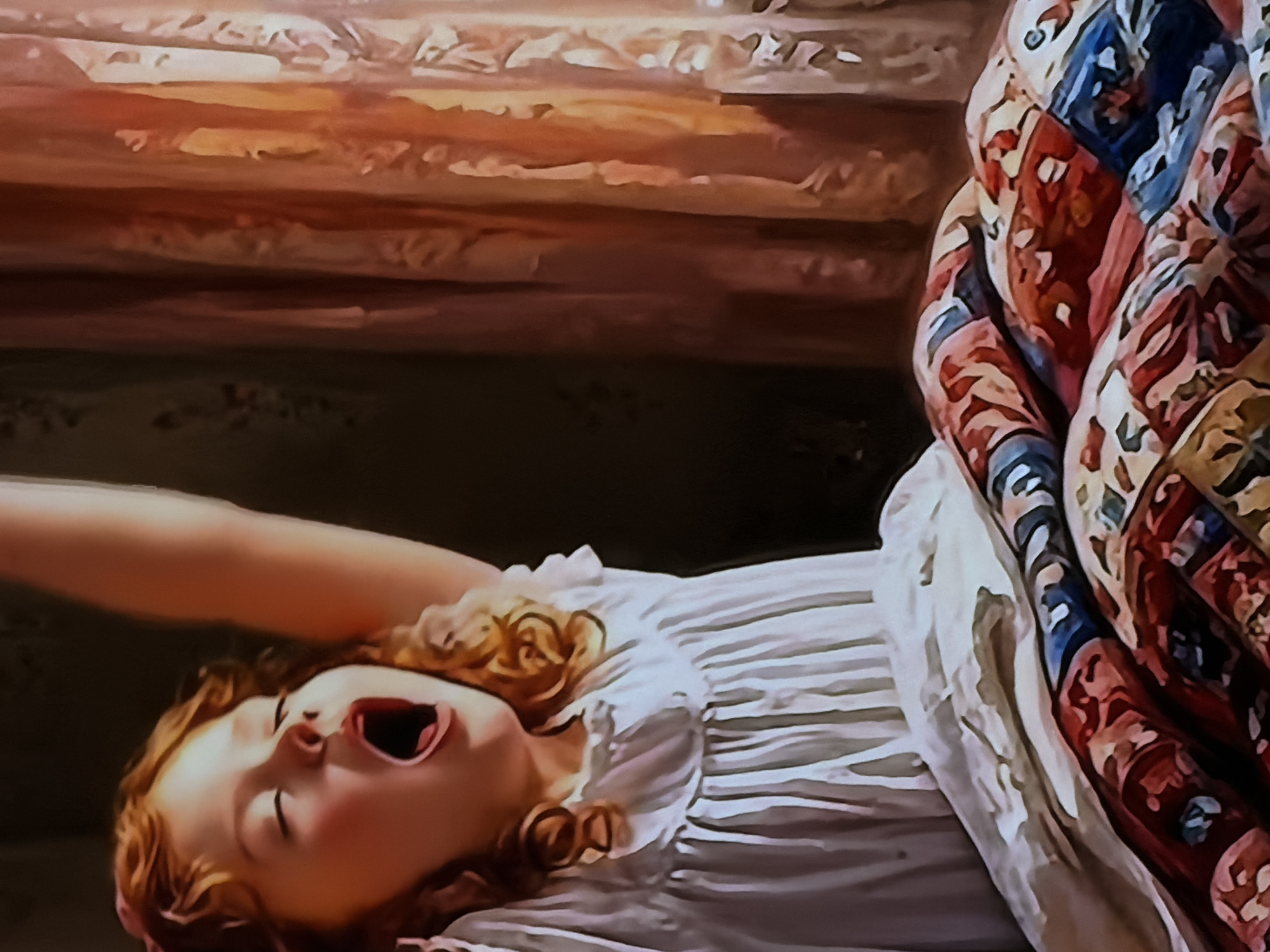This is a painterly image depicting a young child, likely a girl, lying on a bed or sleeping surface. The child has reddish-blonde curly hair and fair skin, and is wearing a white dress or nightgown with ruffled details and subtle horizontal stripes. She is captured in the act of yawning widely, with her mouth open and tongue visible, and her eyes nearly closed. One arm is raised and stretched above her head, indicating a stretch.
To the right side of the image, a colorful, patterned quilt or blanket covers part of the child and the bed. The quilt features geometric and possibly floral designs in shades of red, blue, cream, and brown. The background behind the child appears to be a dimly lit, dark brown surface, possibly a wall or headboard, above which is a lighter, textured area resembling wooden beams or paneling. The overall setting suggests an indoor space, likely a bedroom. The act of yawning and stretching implies the time of day is either morning, just after waking, or evening, indicating tiredness before sleep. No text is visible in the image.
