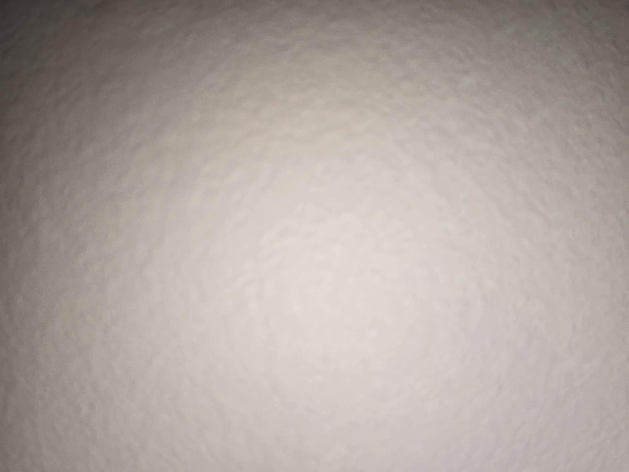 The image is an out-of-focus, close-up shot of a textured, light-colored surface. The texture appears somewhat rough and uneven, with subtle variations in shade and light. There are no discernible objects, people, or a recognizable environment within the frame, making it impossible to determine a specific location within Ulan-Ude, Russia, or any other place. The image lacks any details that could be used for forensic analysis or scene description.
