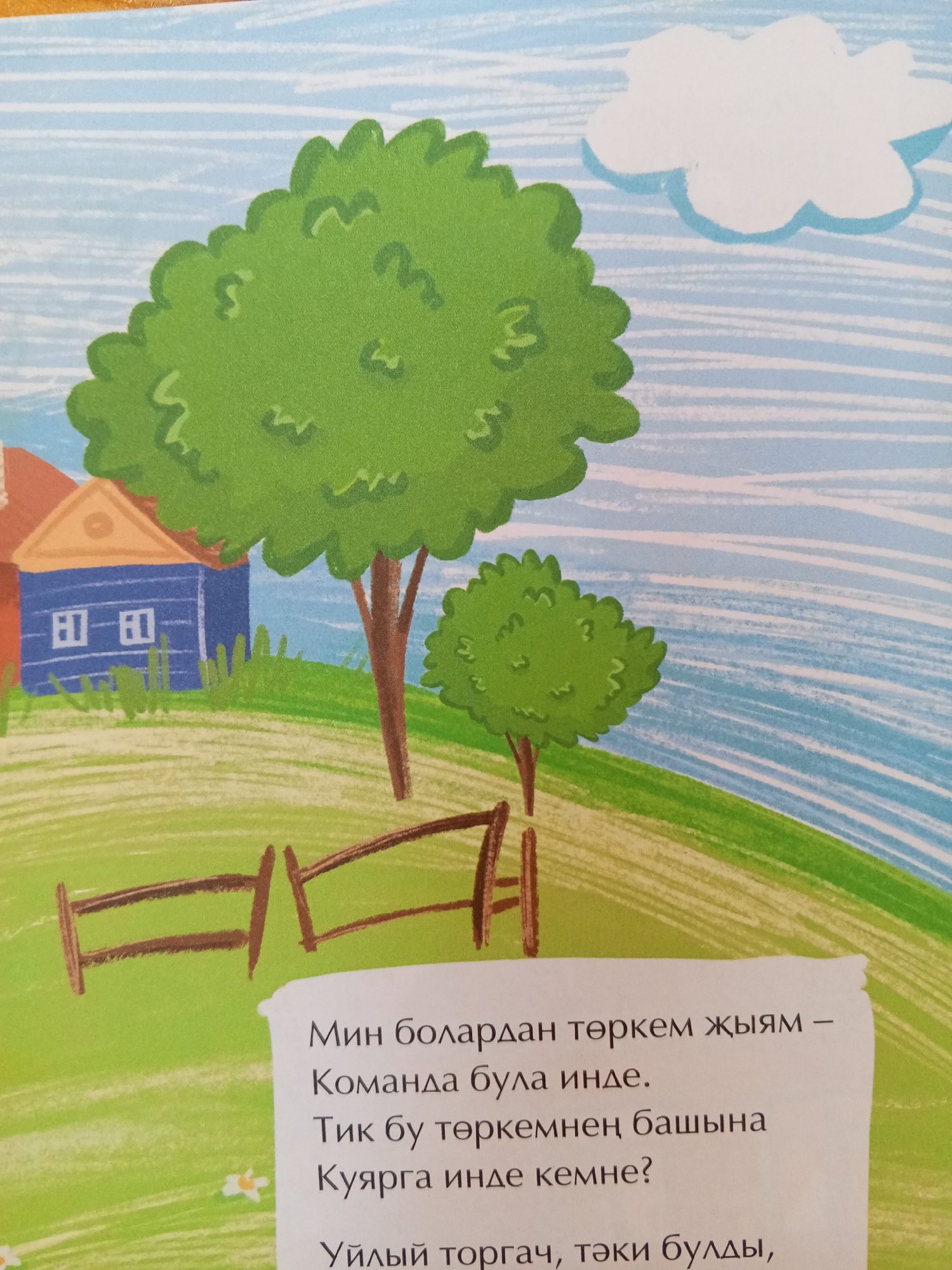 The image is an illustration from a children's book, depicting a pastoral scene with a blue house, green trees, and a wooden fence. The text on the right is in a Cyrillic-based alphabet, likely Tatar, and describes the scene. The illustration style is whimsical and colorful, with soft lines and broad strokes. The sky is depicted as blue with white, puffy clouds and horizontal white lines suggesting wind or movement. There are no people visible in the illustration. The location in Chistopol, Russia, is not explicitly indicated within the image itself.