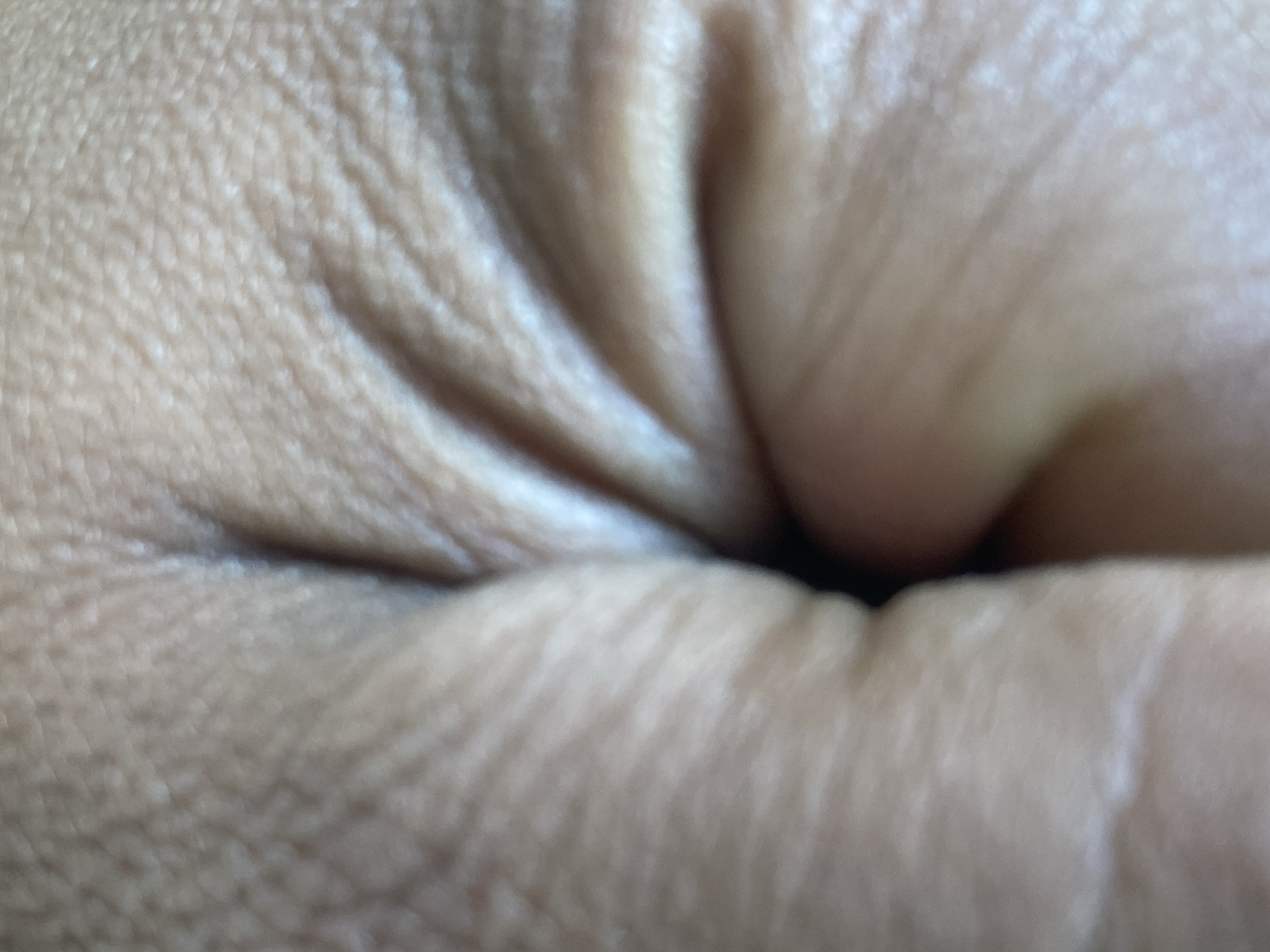 The image shows a close-up of human skin, likely from a hand clenched into a fist. The skin is light brown in color and shows wrinkles and pores. There is a dark area visible between the folds of skin. There is no information in the image that would suggest it was taken in Bukhara, Uzbekistan, or any information about a city, people, actions, objects, or the environment.