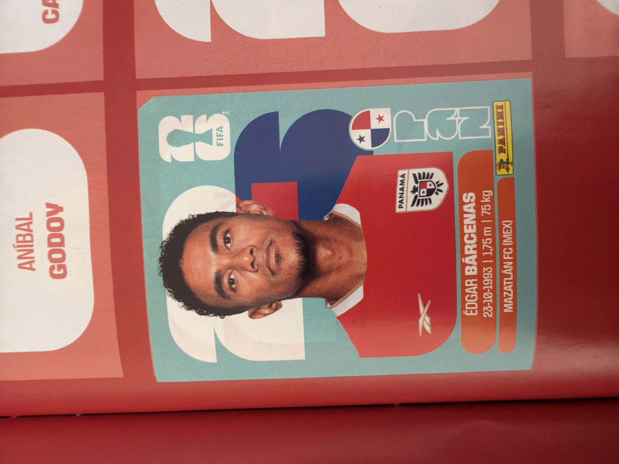 The image shows a close-up of a page from a Panini sticker album, featuring a sticker of a soccer player. The player, Édgar Bárcenas, is shown in a red jersey with the Panamanian crest. Text below the player's image provides his birthdate (23-10-1993), height (1.75 m), weight (75 kg), and club (Mazatlán FC (MEX)). A Panini logo is visible in the bottom right corner of the sticker. The background of the page is red with large, stylized numbers "2" and "3" in a teal color, and the FIFA logo. The image is taken from an upward angle. There is no information in the image to suggest any connection to Zlatitrap, Bulgaria.