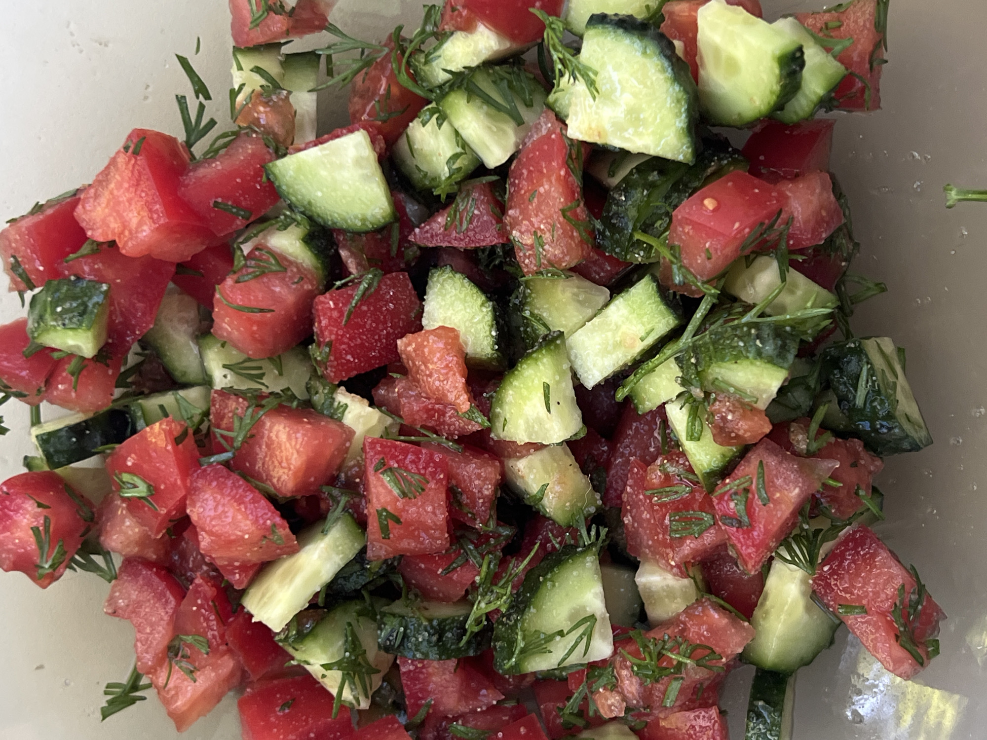 The image shows a close-up of a salad. The salad contains diced tomatoes and cucumbers, garnished with dill. The origin of the image is unknown, and there is no information to place the image in the city of Chaikovsky, Russia.