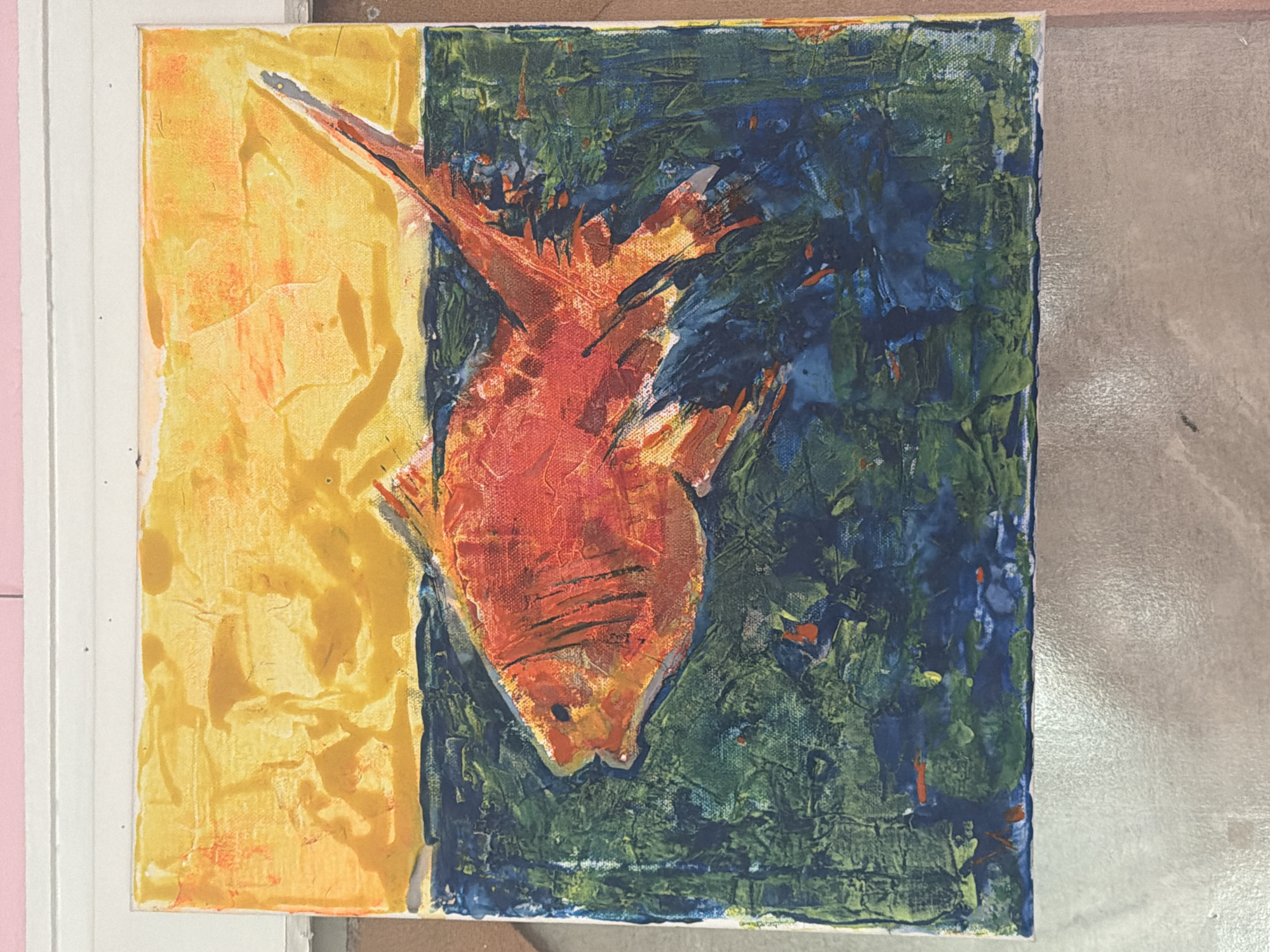 The primary subject of this media file is an abstract painting featuring a fish. The artwork is characterized by its heavily textured surface, indicating the use of thick paint and impasto techniques.
The central figure is a fish, rendered primarily in vibrant shades of orange and red, with subtle yellow and dark outlines. It is positioned diagonally across the canvas, with its head pointing towards the lower left and its tail extending towards the upper right, conveying a sense of energetic movement. The fish itself is depicted with loose, expressive brushstrokes that contribute to its textured appearance.
The background of the painting is starkly divided into two vertical sections. The left side features a bright, textured field of yellow and orange, applied with visible, thick strokes that create a relief-like quality. The right side of the background consists of a dense, heavily textured blend of dark blues and greens, also applied with thick, noticeable brushwork. The fish appears to cross this vertical boundary, uniting the contrasting halves of the background.
There is no specific activity or event taking place other than the implied dynamic posture of the fish. Notable details include the strong textural elements throughout the painting, the vibrant color contrasts, and the abstract, non-realistic style. The painting evokes a lively and dynamic mood through its color palette and expressive application of paint. There is no visible text within the painting. The painting itself does not offer cues regarding time of day, weather, or specific geographical location. The artwork is shown on what appears to be a white frame or mounting, with a light pink surface visible to the left and a neutral gray-brown surface to the right in the surrounding environment of the photograph.