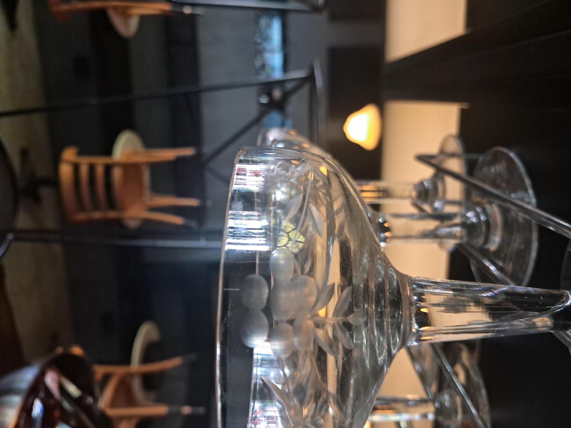 The image depicts a close-up of a row of wine glasses with etched floral designs, possibly arranged on a drying rack, in what appears to be a commercial setting. The background shows blurred chairs and lighting, suggesting a restaurant or bar environment. The location is specified as Vicente López, Argentina.