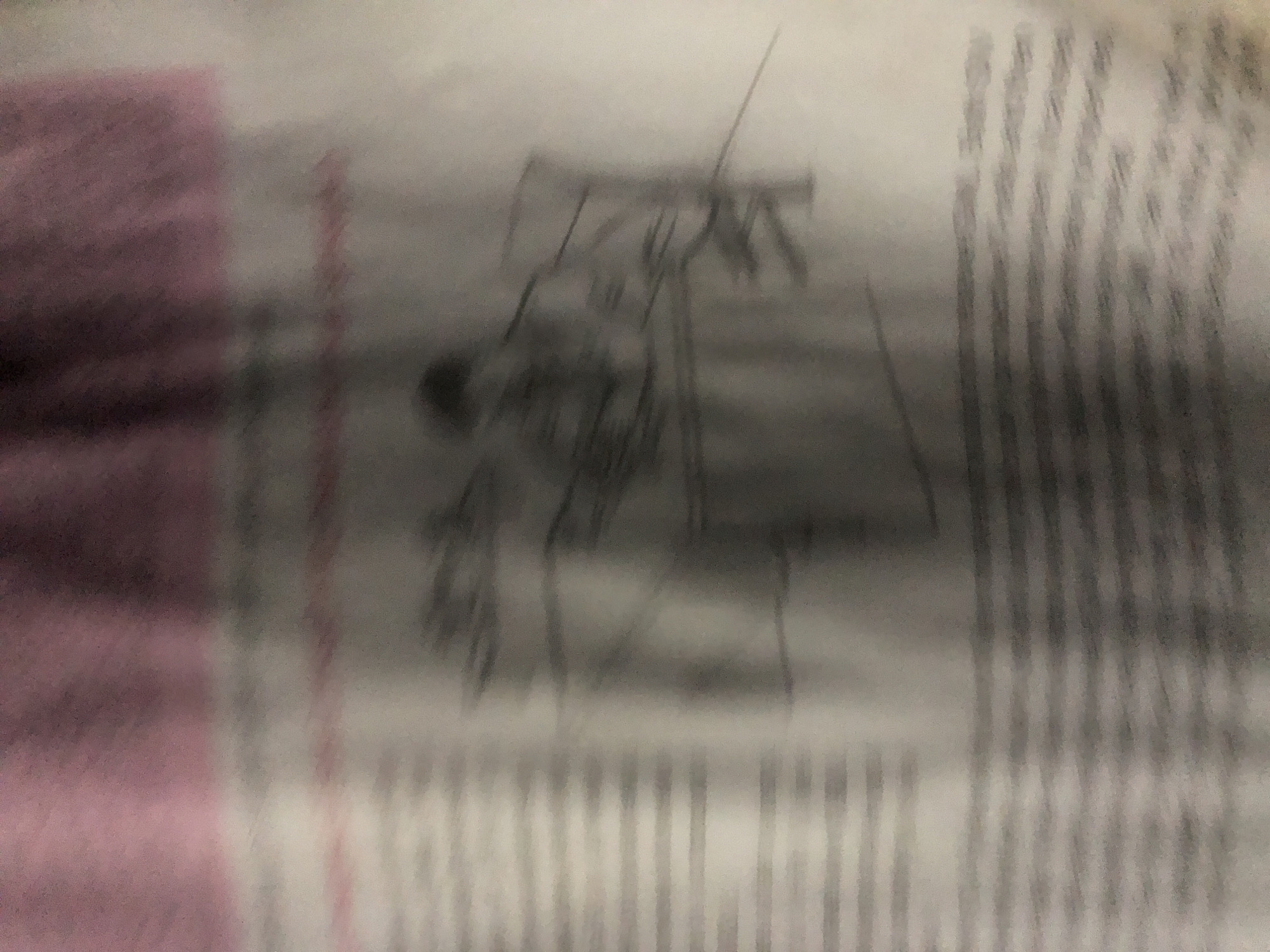 The image is a blurry, low-resolution photograph of what appears to be a page from a book or magazine. The dominant colors are pink, white, and gray. There is a faint illustration or diagram in the center of the image, rendered in dark lines. The text below the illustration is also blurred and unreadable. The background is a solid pinkish color, suggesting a cover or a section of colored paper. The image is heavily out of focus, making it difficult to discern any specific details. There is no information in the image that would allow for its location to be identified, either in Jalingo, Nigeria, or anywhere else.