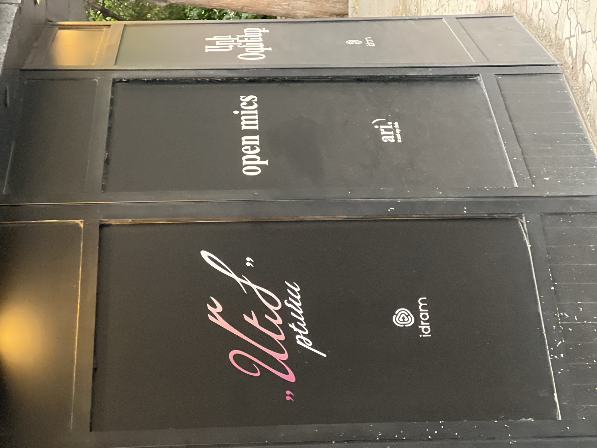 This image depicts a stack of advertisements. The top advertisement reads "Unh Ogitalp" and includes the "idram" logo. The middle advertisement reads "open mics" and includes the "ari. stand-up club" logo. The bottom advertisement reads "Utis pturu" and includes the "idram" logo. The advertisements are in black frames. The city of Yerevan, Armenia, is not directly apparent from the image.