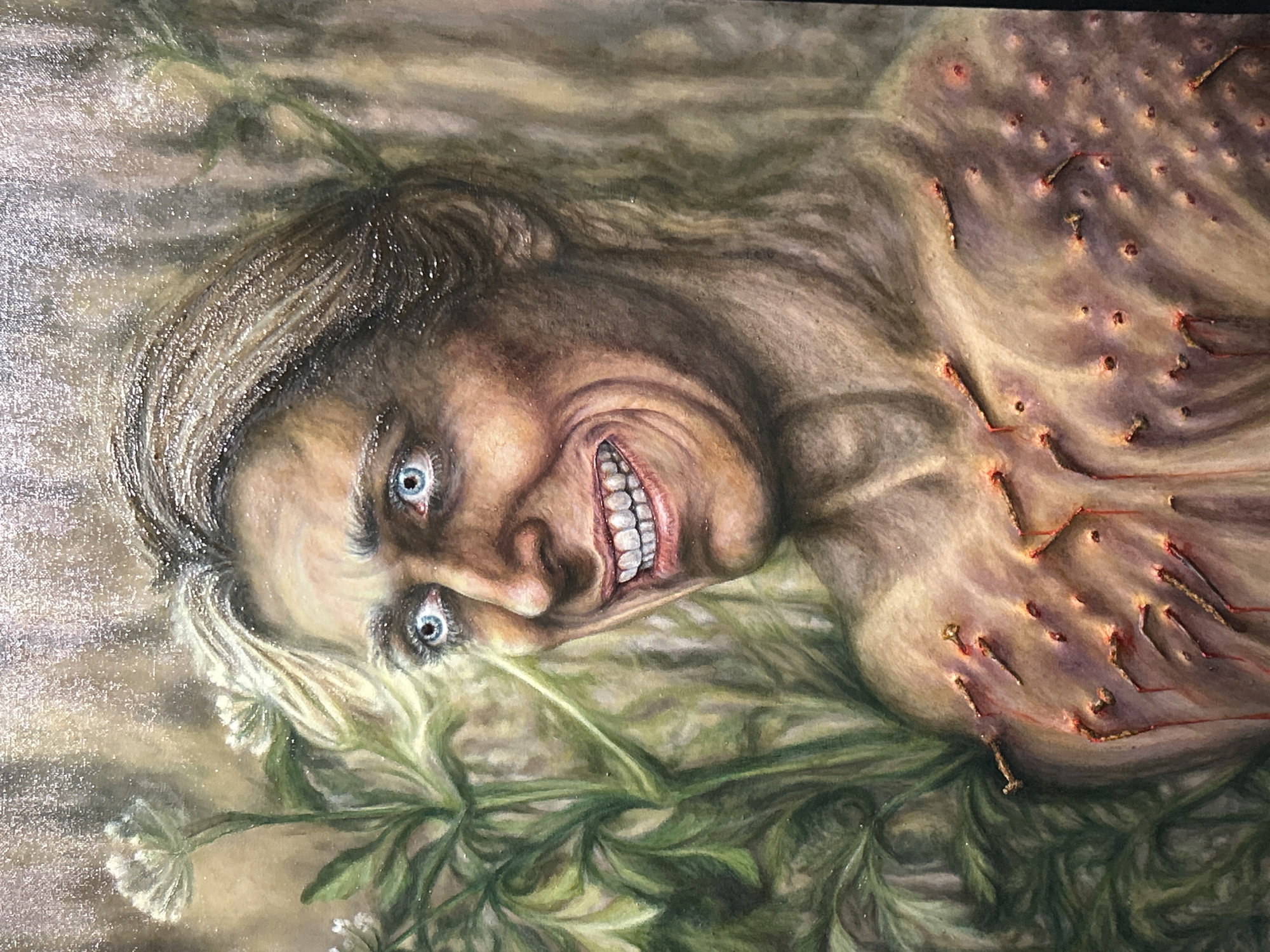 This is a painting depicting a person, likely female, lying amidst green foliage and small white wildflowers. The subject's head is turned towards the viewer, featuring a gaunt face with a striking, unsettling expression. She has wide, piercing blue eyes that stare intently, and her mouth is open in a wide, contorted grin, revealing prominent white teeth. Deep wrinkles radiate from her eyes and mouth, contributing to an impression of distress, madness, or extreme emotion. Her hair is a mix of light brown and gray, appearing dishevelled.
The upper torso and chest of the figure are visible, covered in numerous small, metallic nails or tacks that appear to be embedded directly into the skin. Thin, reddish lines, resembling thread or dried blood, connect some of these tacks, forming a disturbing, intricate pattern. The skin in these areas appears discolored and inflamed around the points of insertion. The background is a muted, abstract blend of greens and browns, suggesting a natural outdoor setting, possibly a forest floor or an overgrown garden.
The painting evokes a strong sense of horror, psychological distress, or macabre fantasy. There is no visible text in the image.